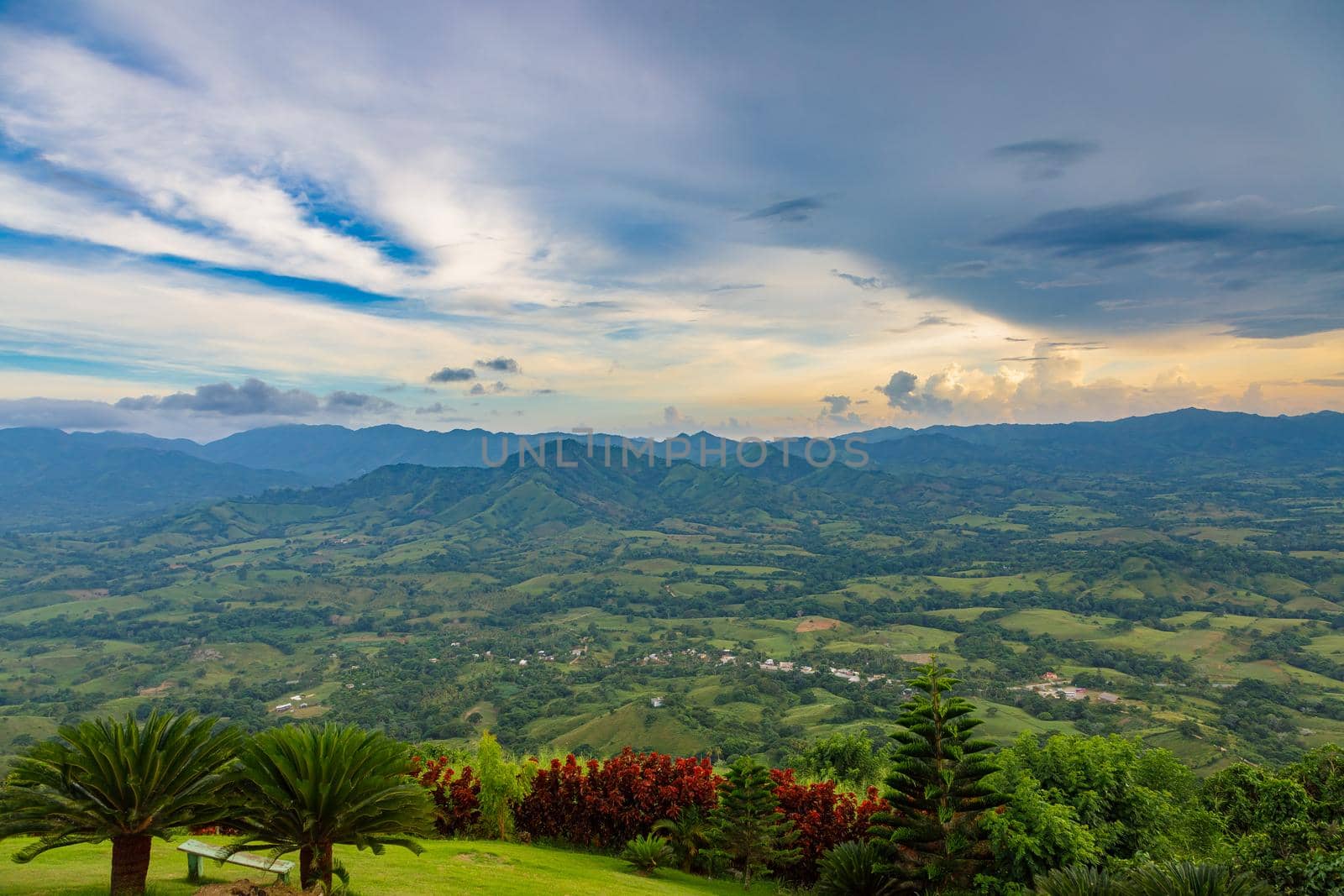 View from a large mountain to a valley with a lake in the Dominican Republic. Setting sun. Around greenery and red bushes