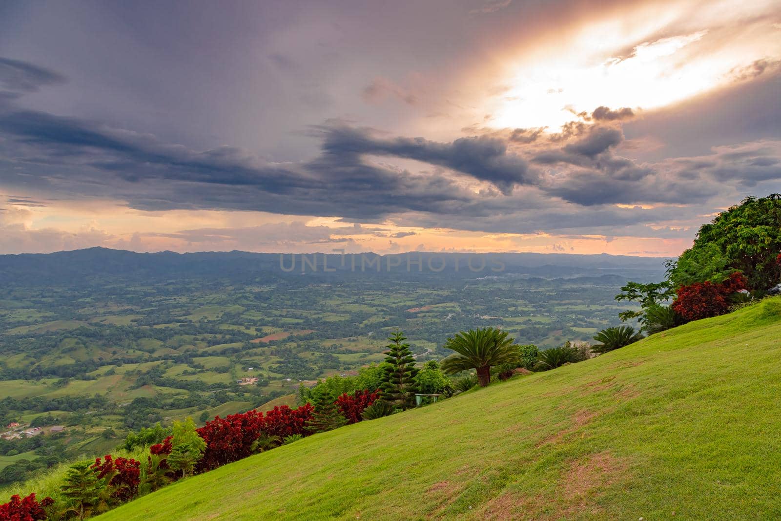View from a large mountain to a valley with a lake in the Dominican Republic. Setting sun. Around greenery and red bushes