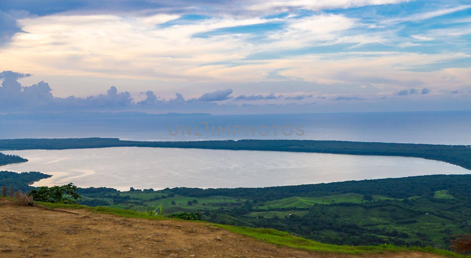 View from a large mountain to a valley with a lake in the Dominican Republic. Setting sun. Around greenery and red bushes