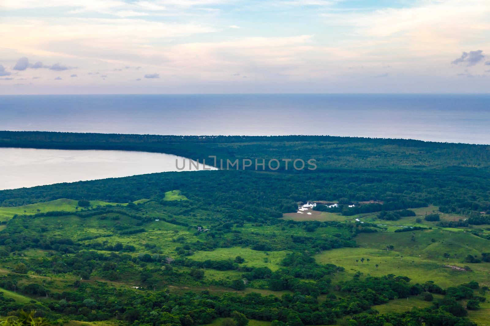View from a large mountain to a valley with a lake in the Dominican Republic. Setting sun. Around greenery and red bushes