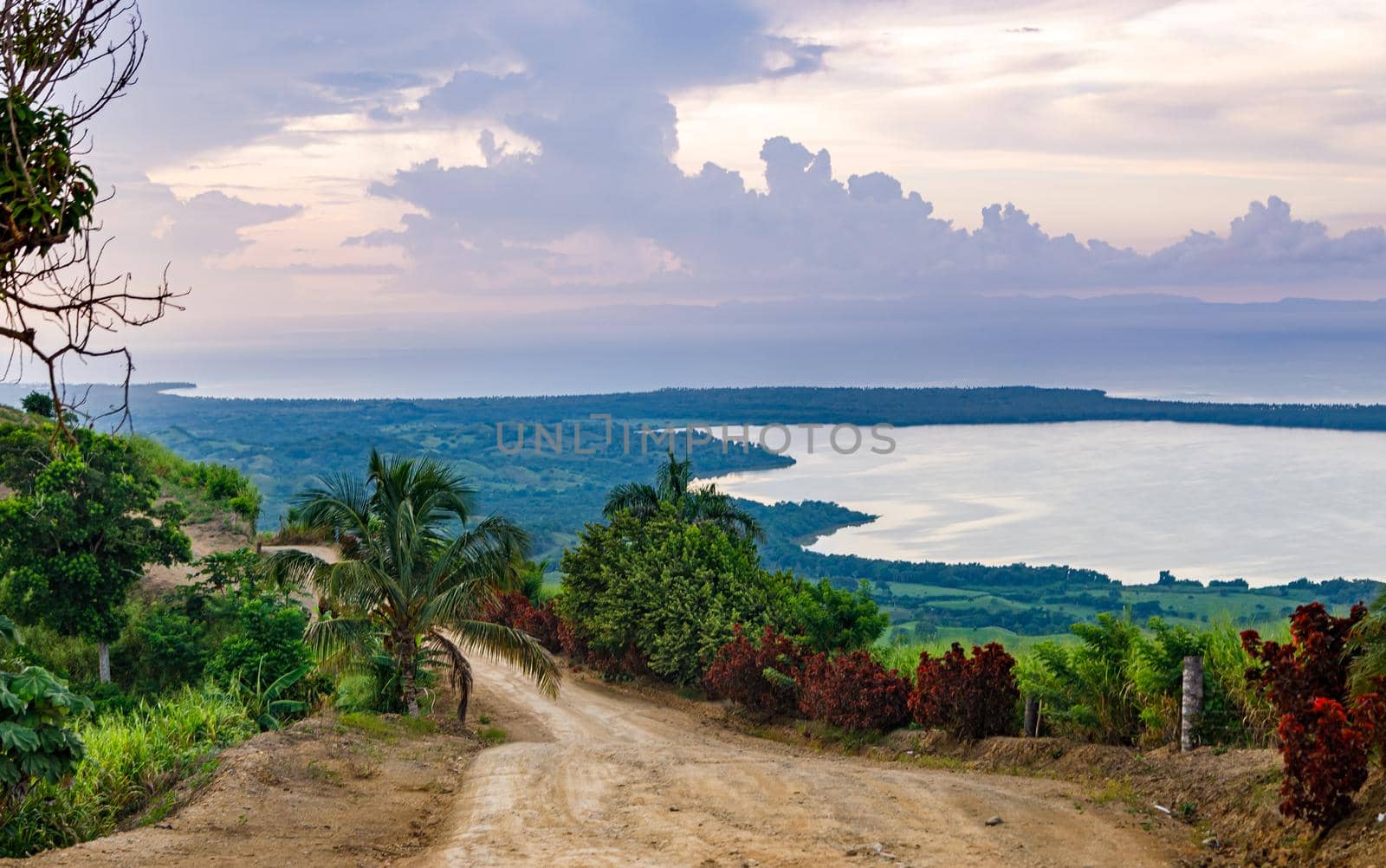 View from a large mountain to a valley with a lake in the Dominican Republic. Setting sun. Around greenery and red bushes