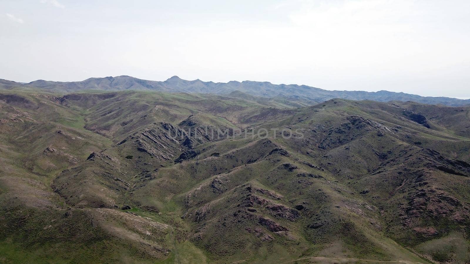 View of green hills and gorges with rocks. In the distance you can see the mountains, the river, the road. Hills covered with grass. Small gorges. Pure nature. Top view from the drone. Kazakhstan.