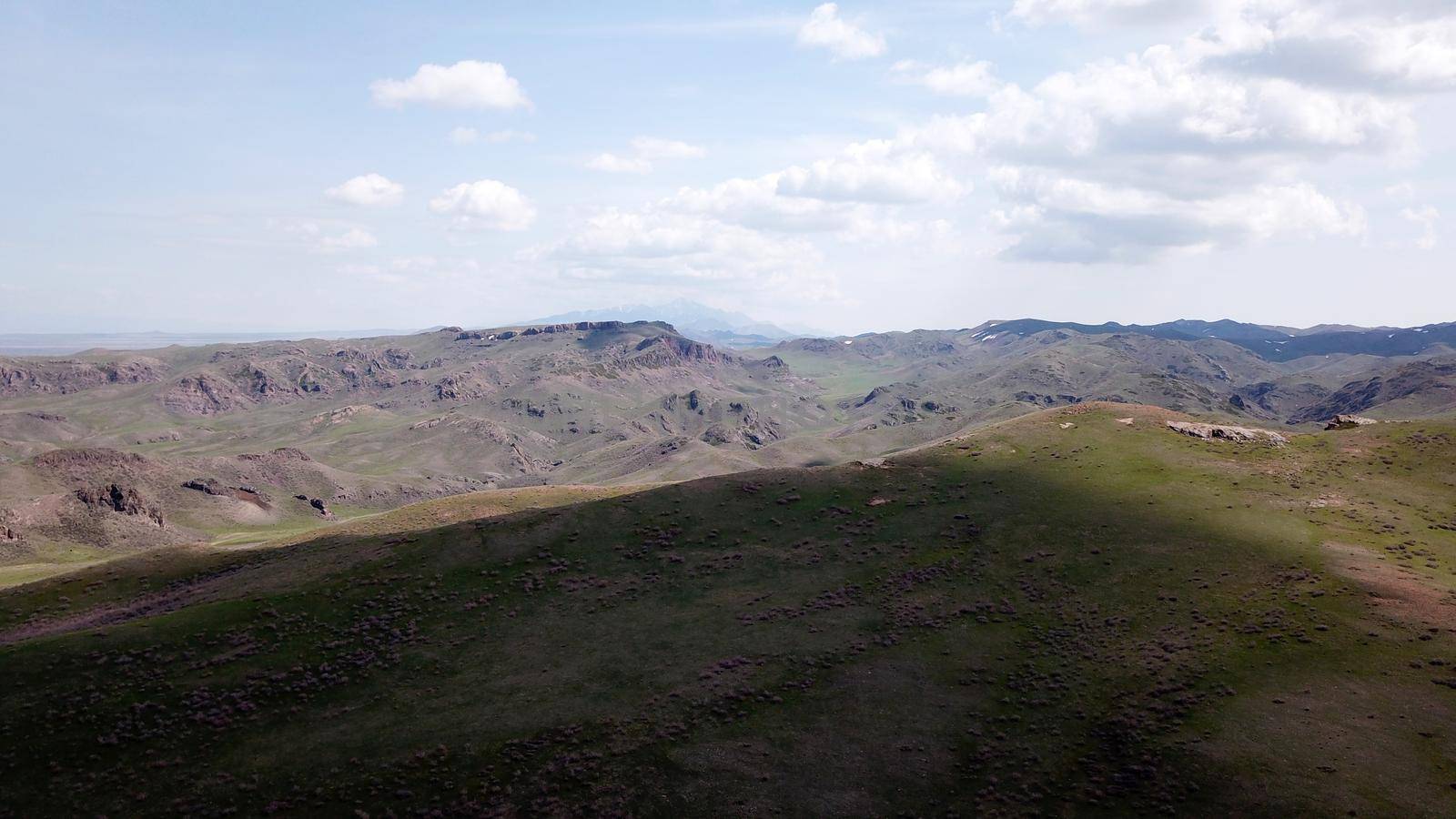 The shadow of the clouds runs over the green hills. In the distance you can see the mountains, the river, the road. Hills covered with grass. Small gorges. Pure nature. Top view from drone. Kazakhstan