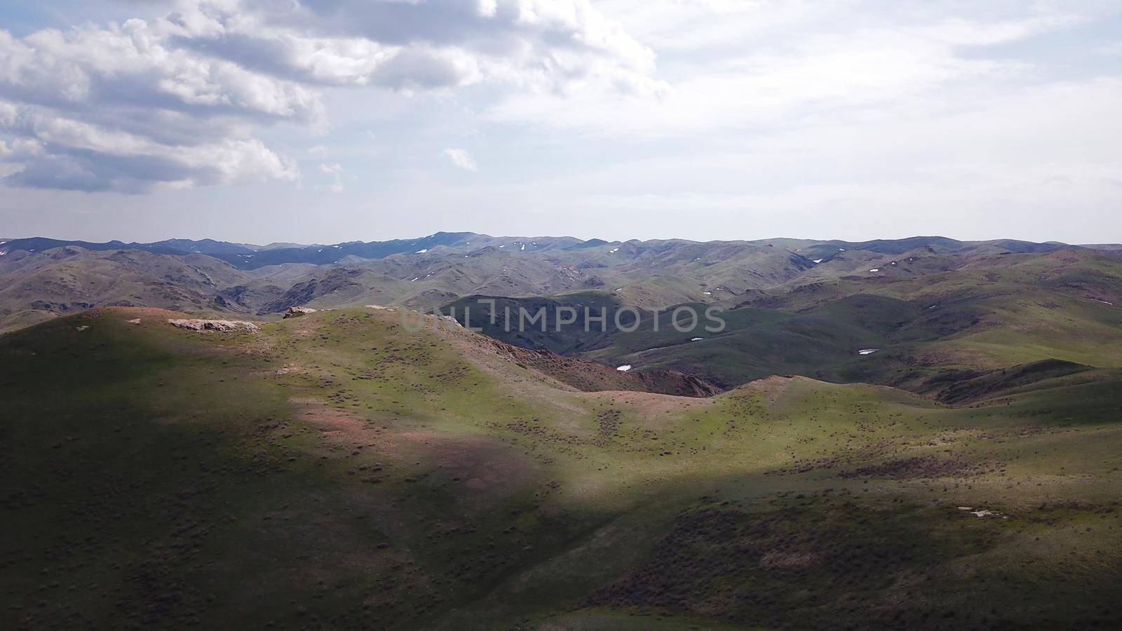 The shadow of the clouds runs over the green hills. In the distance you can see the mountains, the river, the road. Hills covered with grass. Small gorges. Pure nature. Top view from drone. Kazakhstan