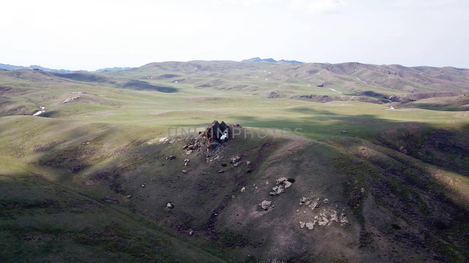 The shadow of the clouds runs over the green hills. In the distance you can see the mountains, the river, the road. Hills covered with grass. Small gorges. Pure nature. Top view from drone. Kazakhstan