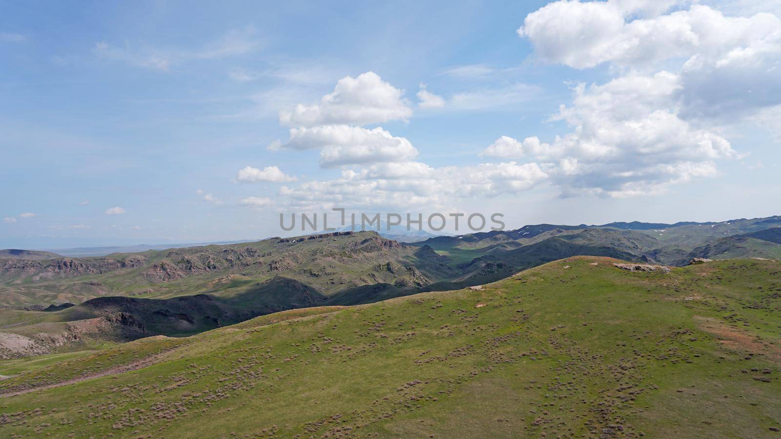 The shadow of the clouds runs over the green hills. In the distance you can see the mountains, the river, the road. Hills covered with grass. Small gorges. Pure nature. Top view from drone. Kazakhstan