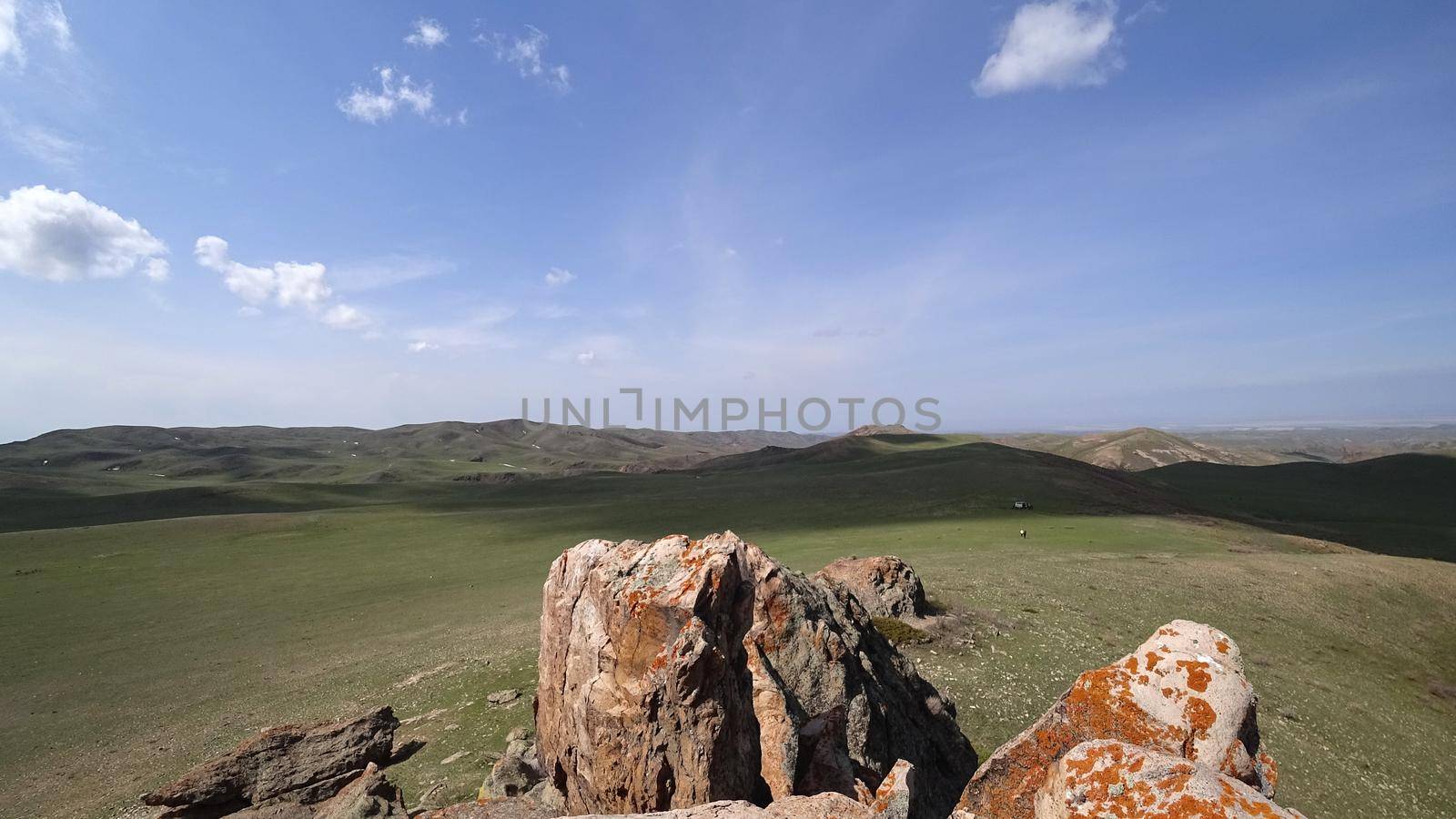 The shadow of the clouds runs over the green hills. In the distance you can see the mountains, the river, the road. Hills covered with grass. Small gorges. Pure nature. Top view from drone. Kazakhstan