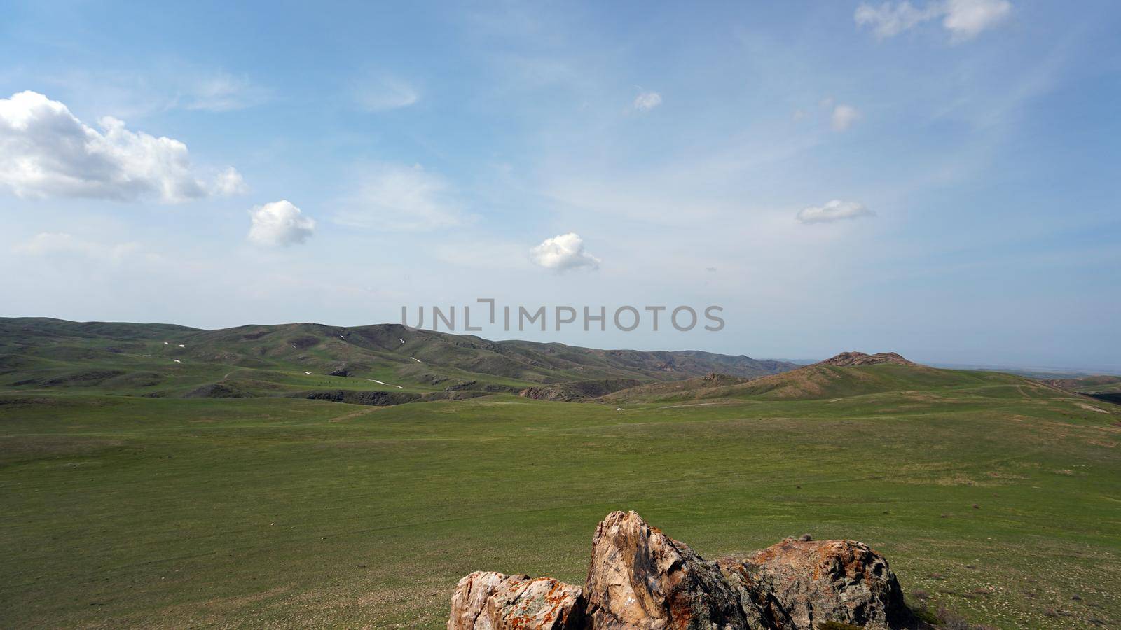 The shadow of the clouds runs over the green hills. In the distance you can see the mountains, the river, the road. Hills covered with grass. Small gorges. Pure nature. Top view from drone. Kazakhstan