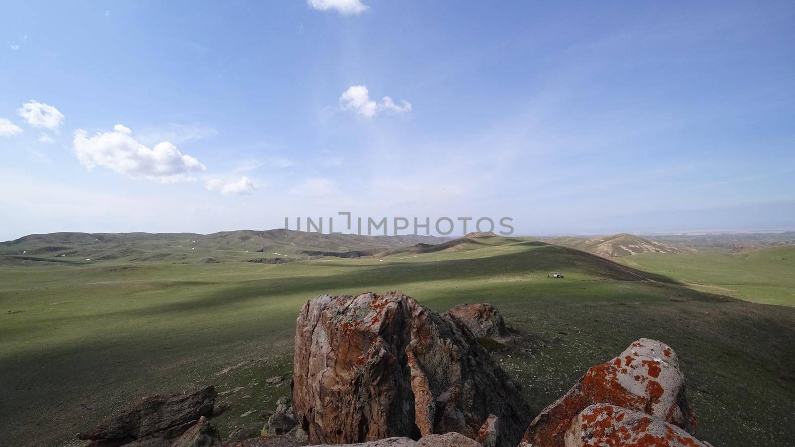 The shadow of the clouds runs over the green hills. In the distance you can see the mountains, the river, the road. Hills covered with grass. Small gorges. Pure nature. Top view from drone. Kazakhstan