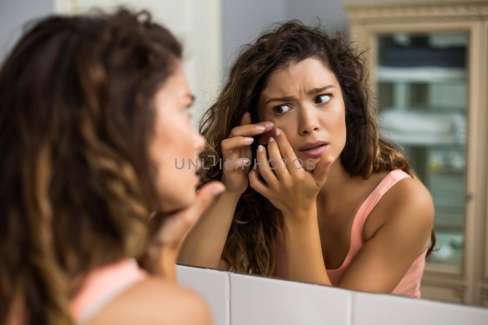 Beautiful woman squeezing pimple in the bathroom.