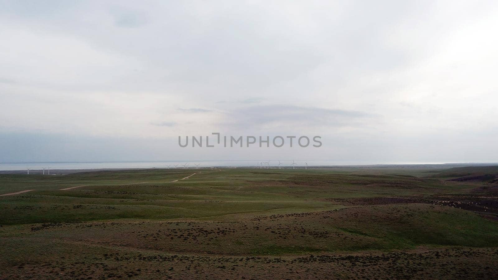 Windmills stand in the middle of green fields. Clean energy is generated. Cloudy weather, dark clouds. Green grass grows. High hills in the distance. Top view from drone. Industrial farm of Kazakhstan