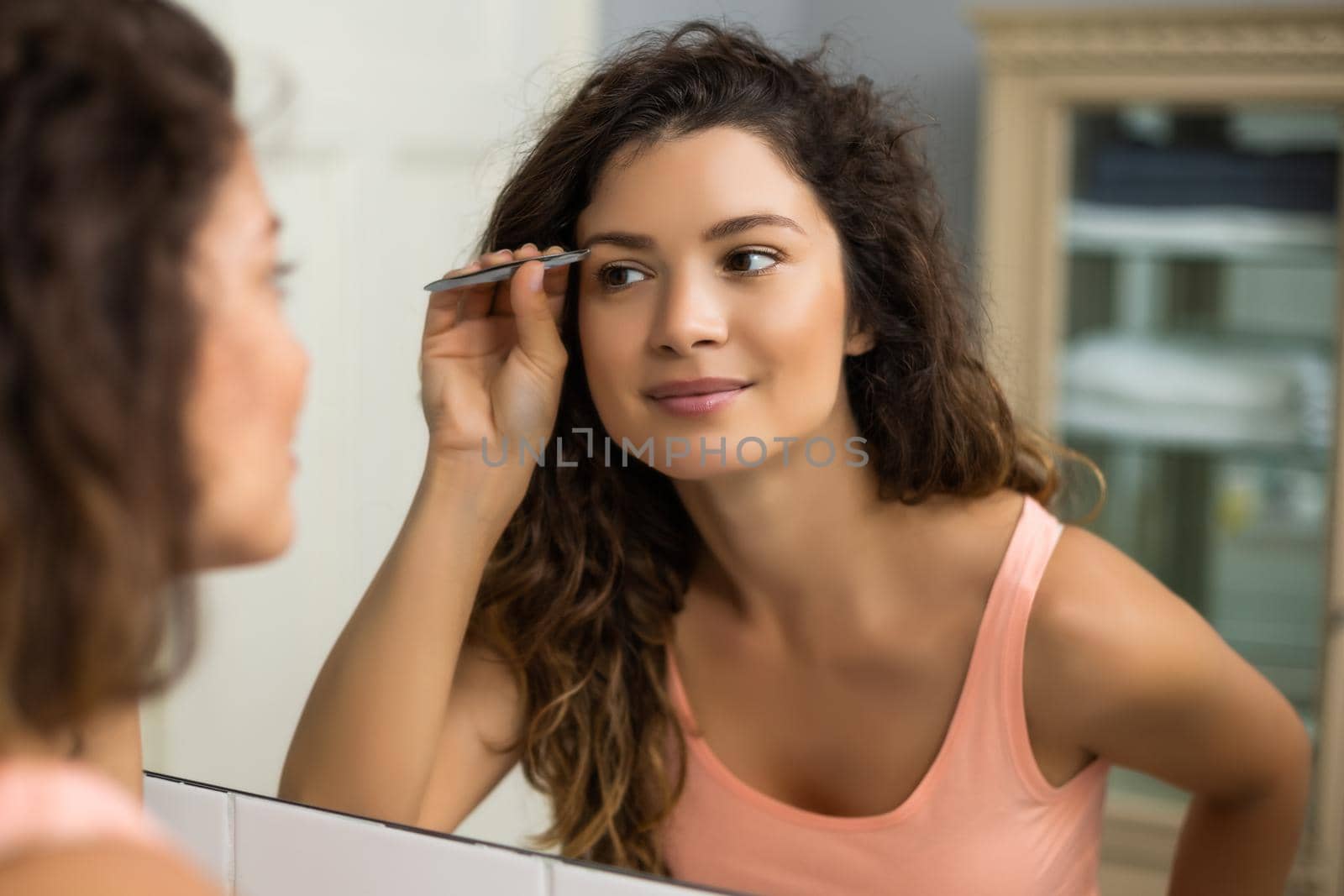 Beautiful woman plucking eyebrows in bathroom.