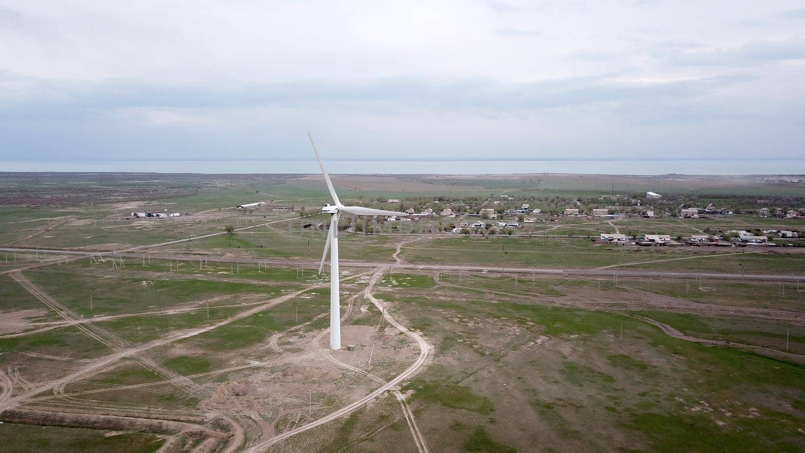 Windmills stand in the middle of green fields. Clean energy is generated. Cloudy weather, dark clouds. Green grass grows. High hills in the distance. Top view from drone. Industrial farm of Kazakhstan