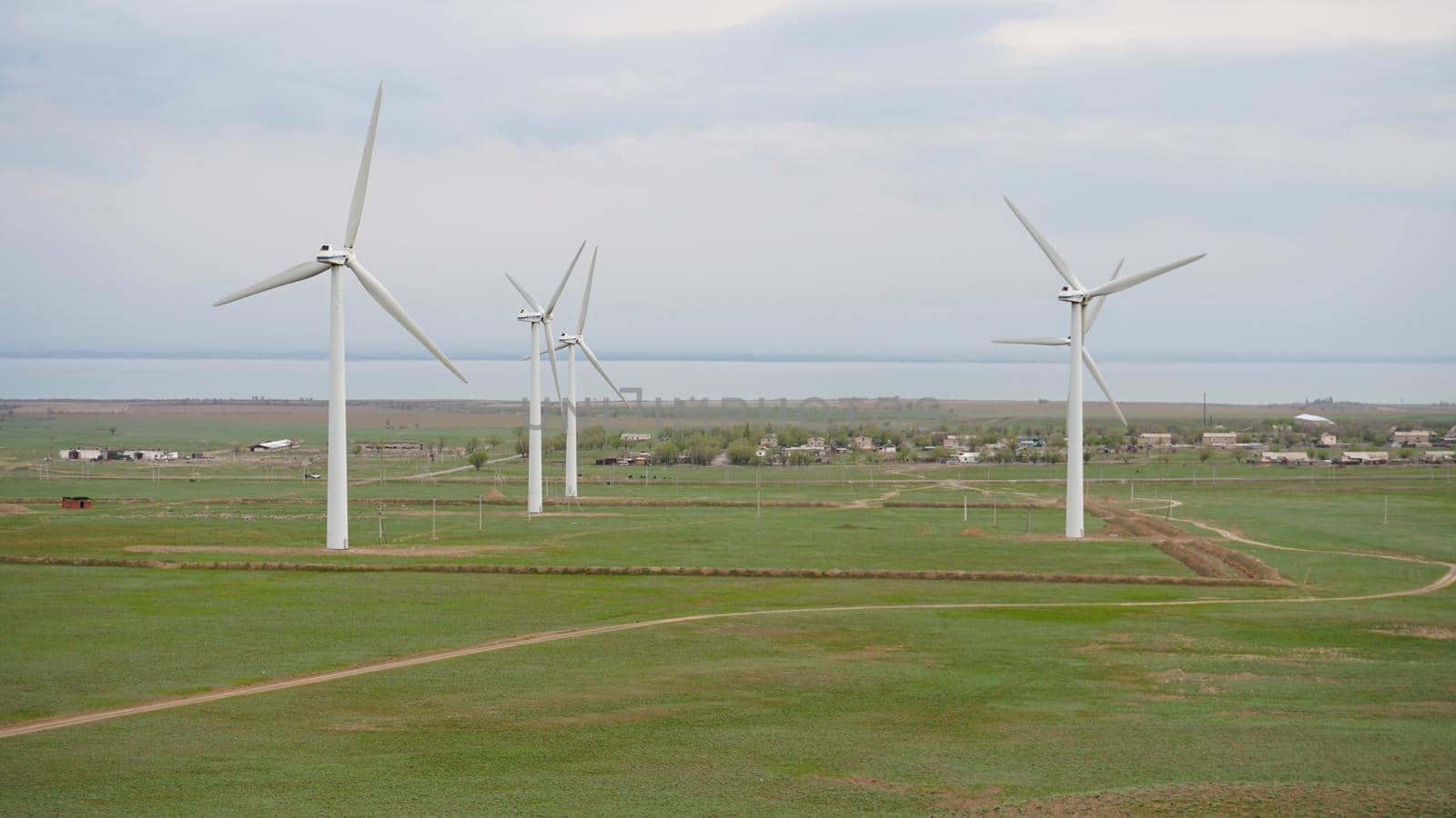 Windmills stand in the middle of green fields. by Passcal