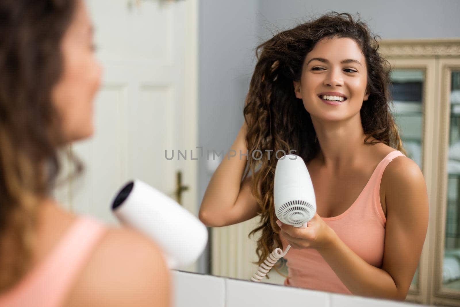 Young woman with gorgeous  curly hair using hairdryer.