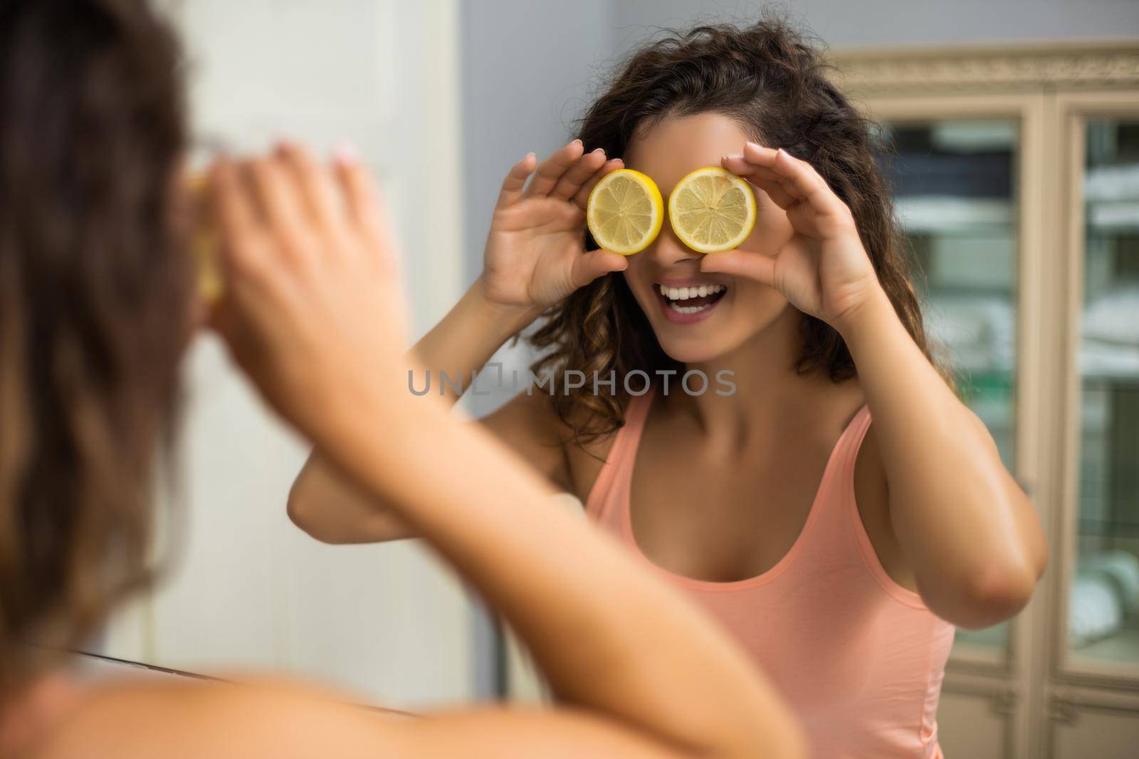 Beautiful woman is covering her eyes with slices of lemon in the bathroom.