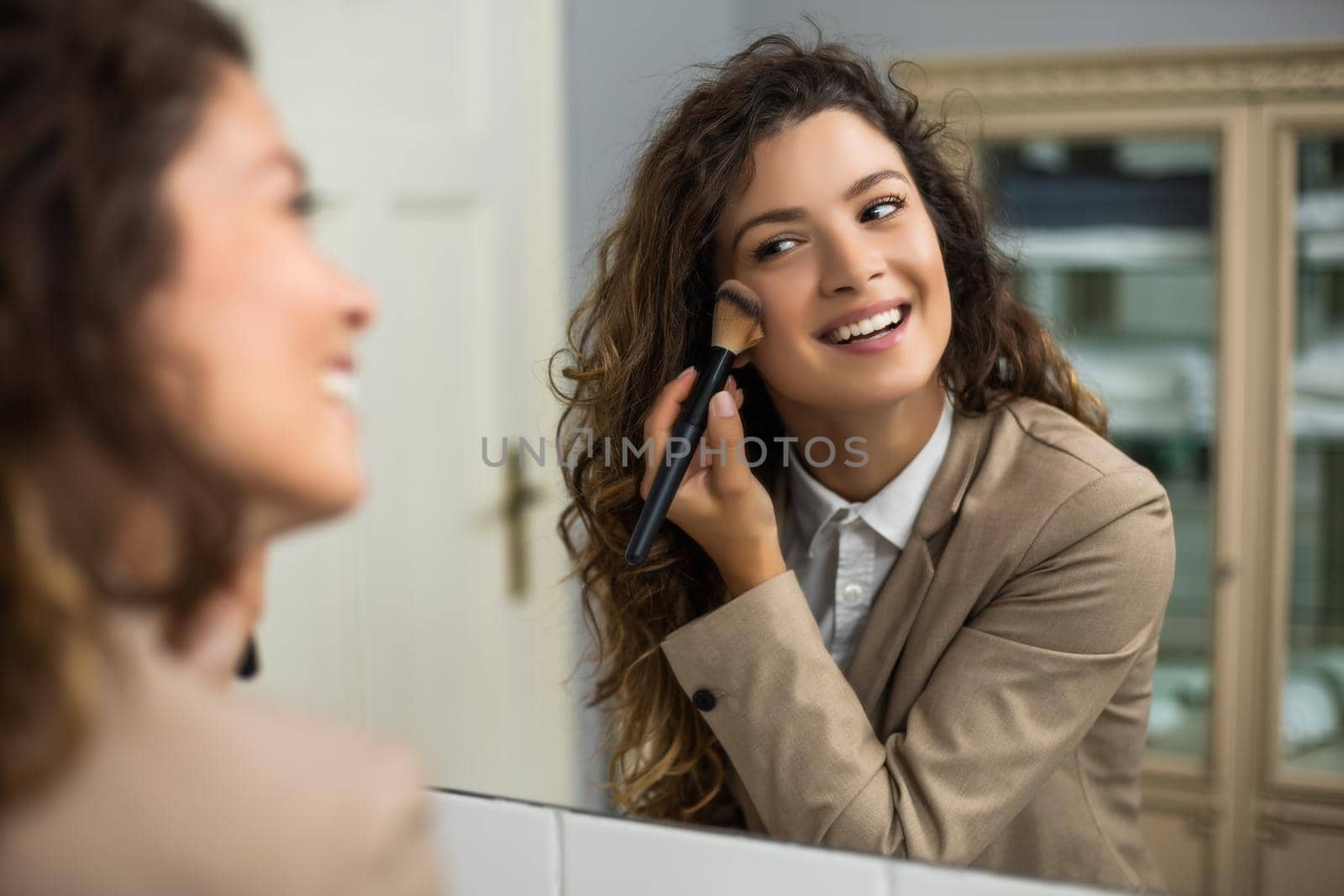 Businesswoman is applying blush while preparing for work.