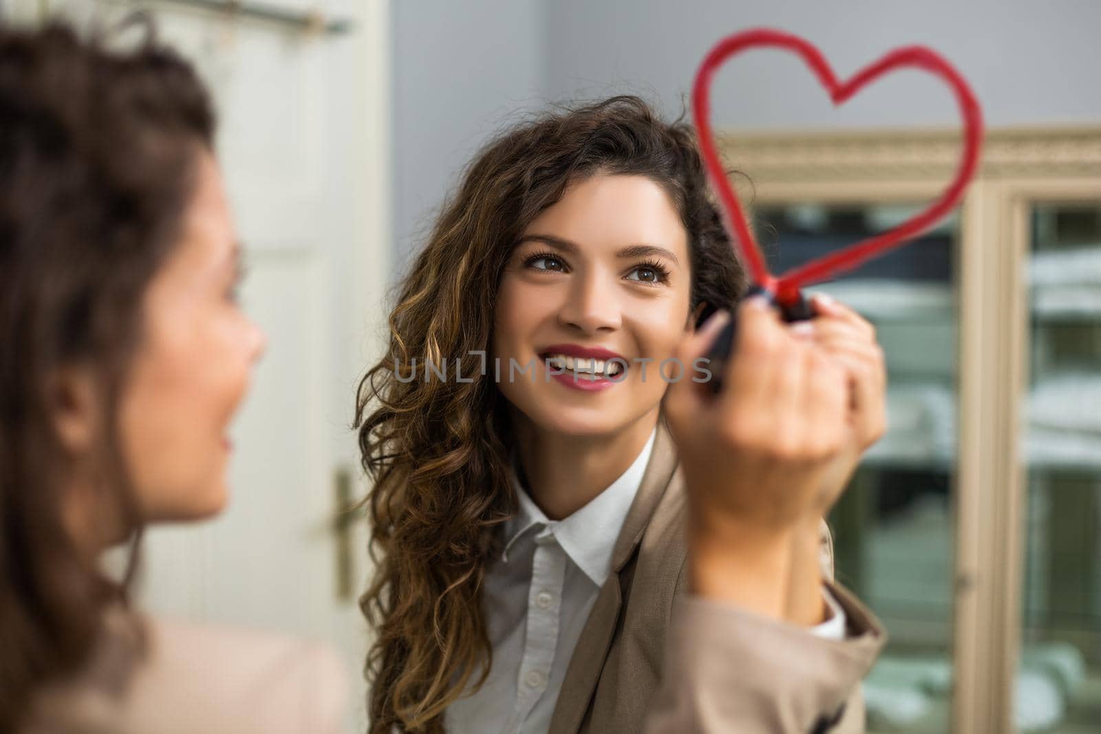 Businesswoman is drawing heart with lipstick on the mirror while preparing for work.