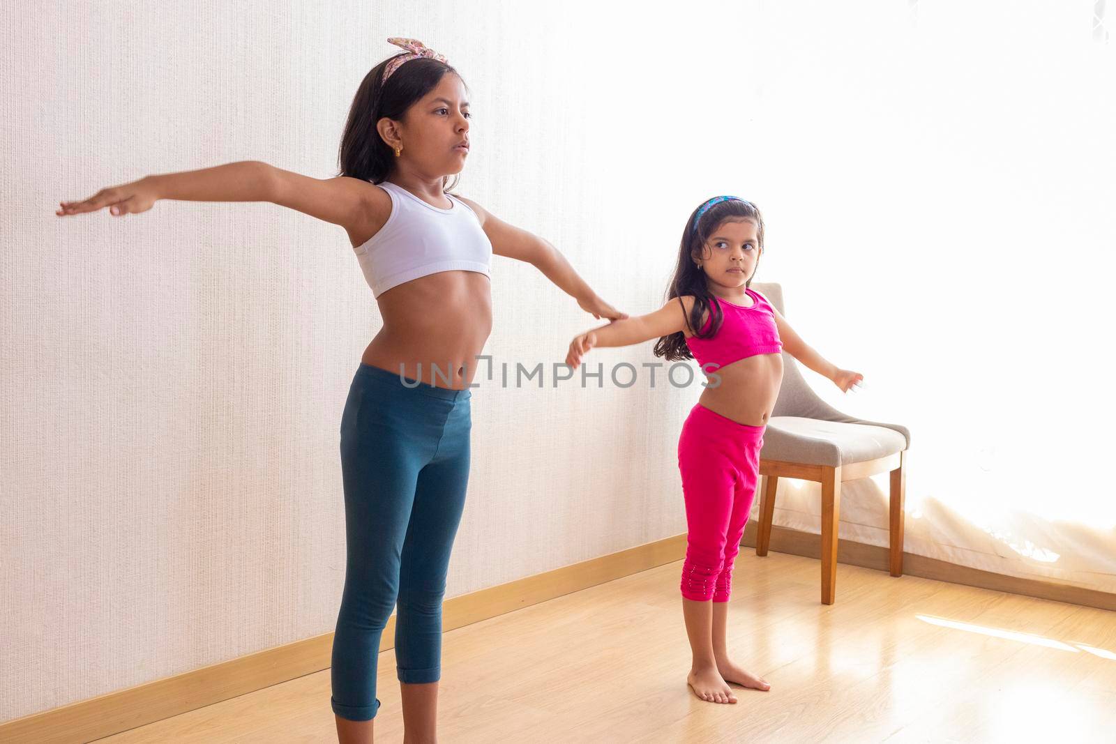 Two little sisters are doing exercise routines in the living roo by eagg13
