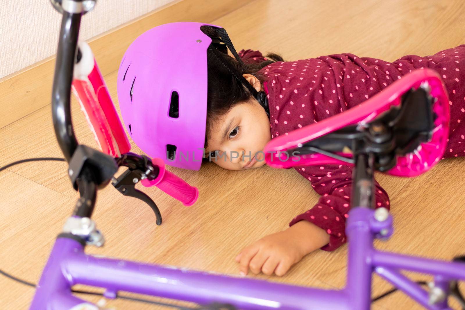 Sad little girl fell to the ground while playing with her bicycle in the house