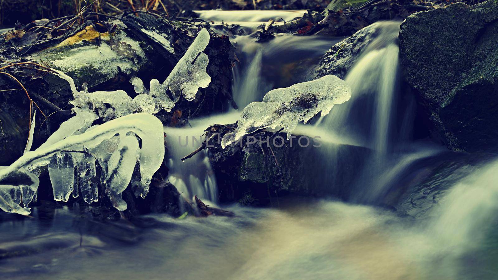 Blurred flowing water in winter creek. Beautiful photo of winter nature in the forest.