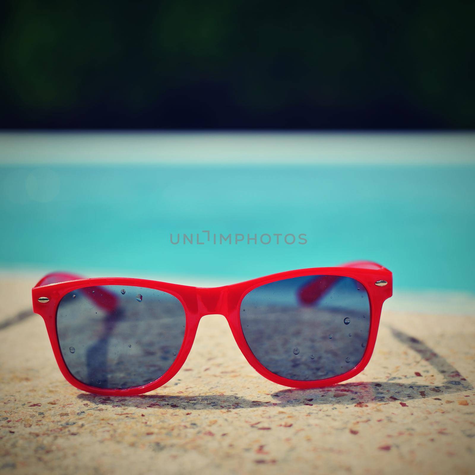 Summer background. Concept for summer and vacation. Red sunglasses by the pool in the background with blue water.