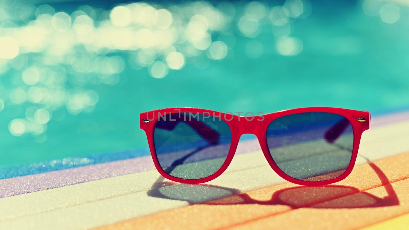 Summer background. Concept for summer and vacation. Red sunglasses by the pool in the background with blue water. by Montypeter