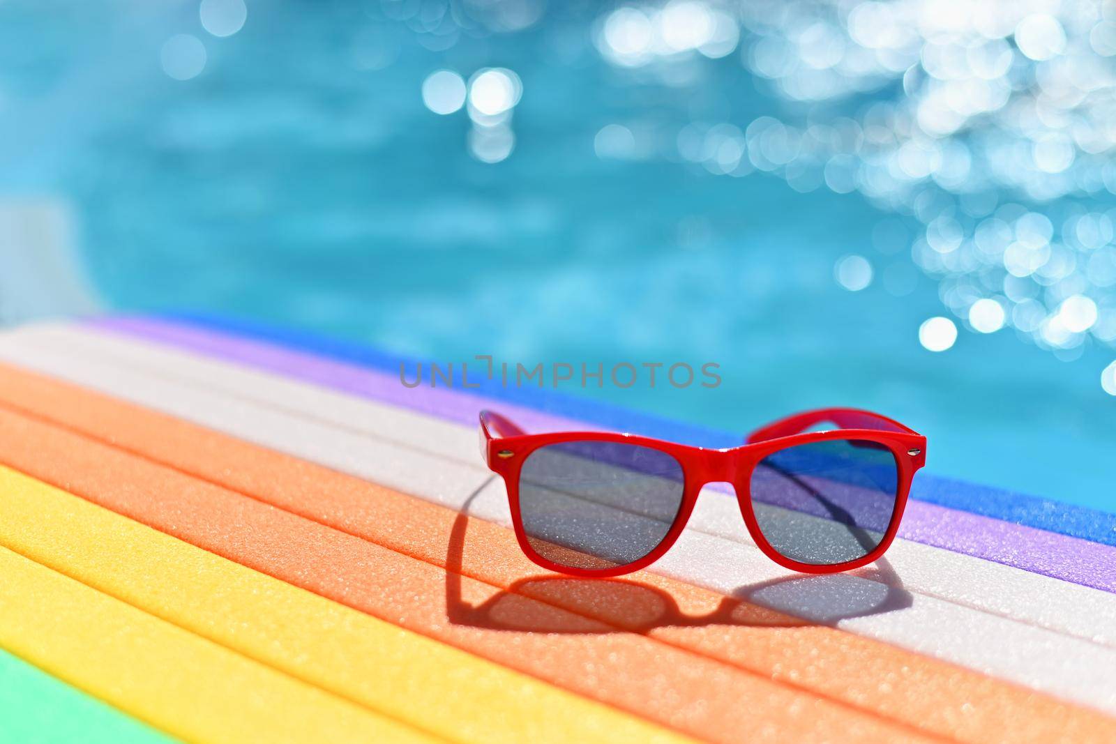 Summer background. Concept for summer and vacation. Red sunglasses by the pool in the background with blue water.