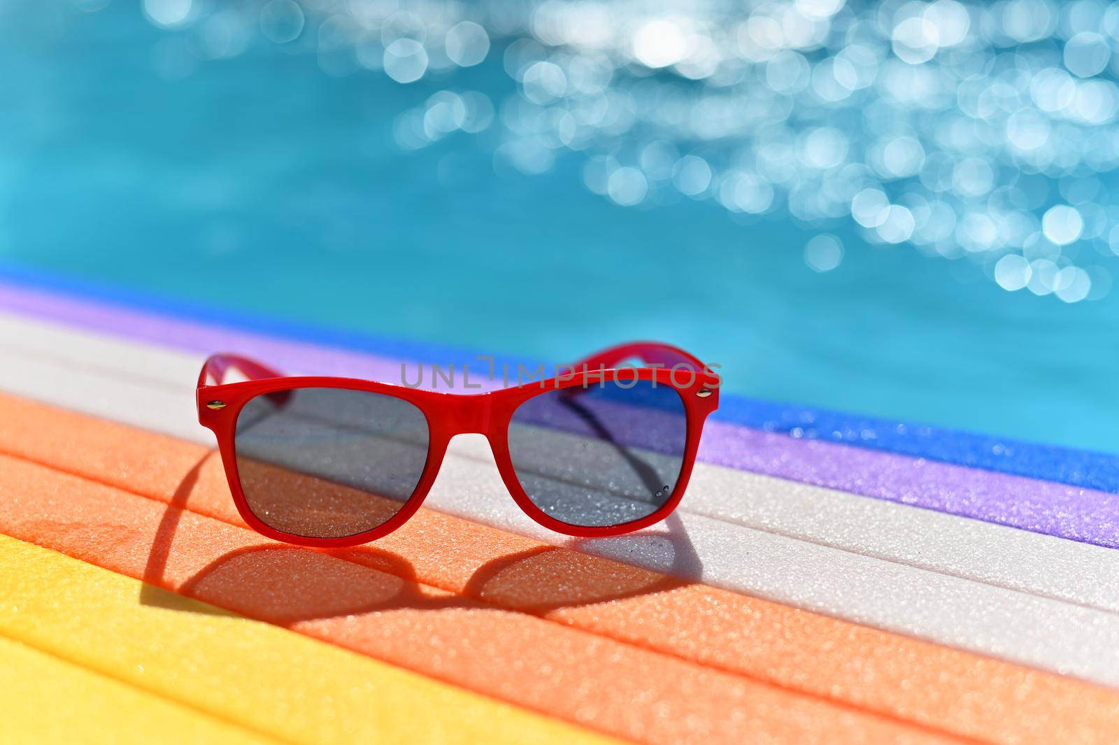 Summer background. Concept for summer and vacation. Red sunglasses by the pool in the background with blue water.