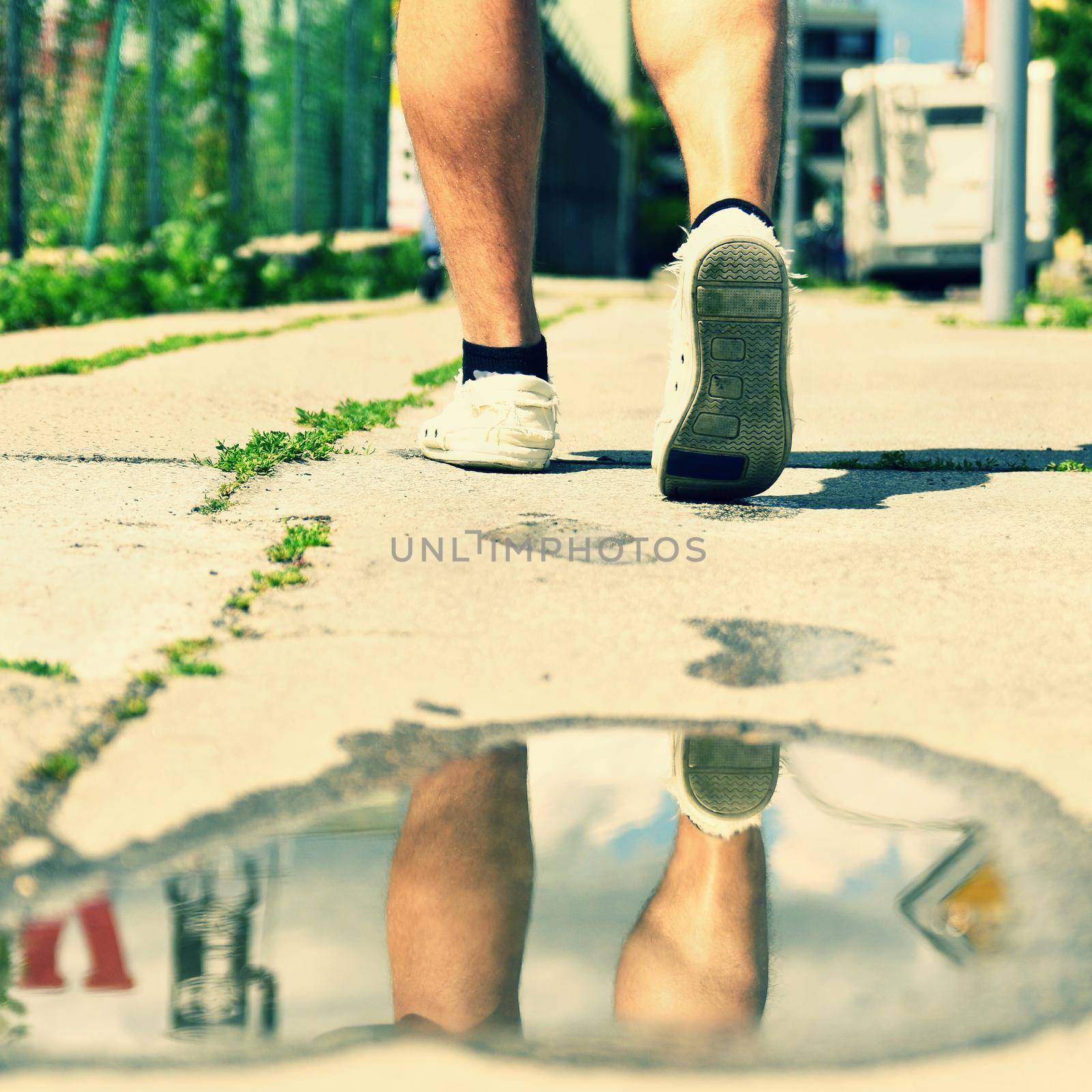 Legs while walking. Reflections in water on the sidewalk. by Montypeter