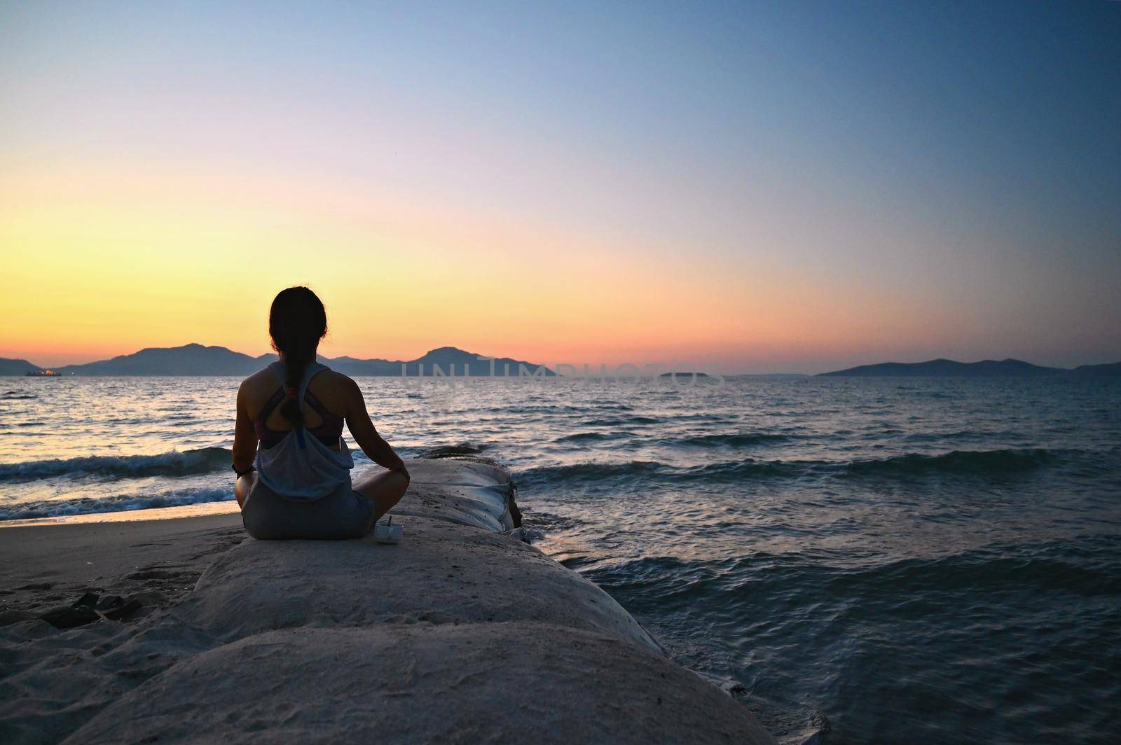 Woman meditates - relaxes at sunset by the sea on the beach. Concept for yoga, health and spa. by Montypeter