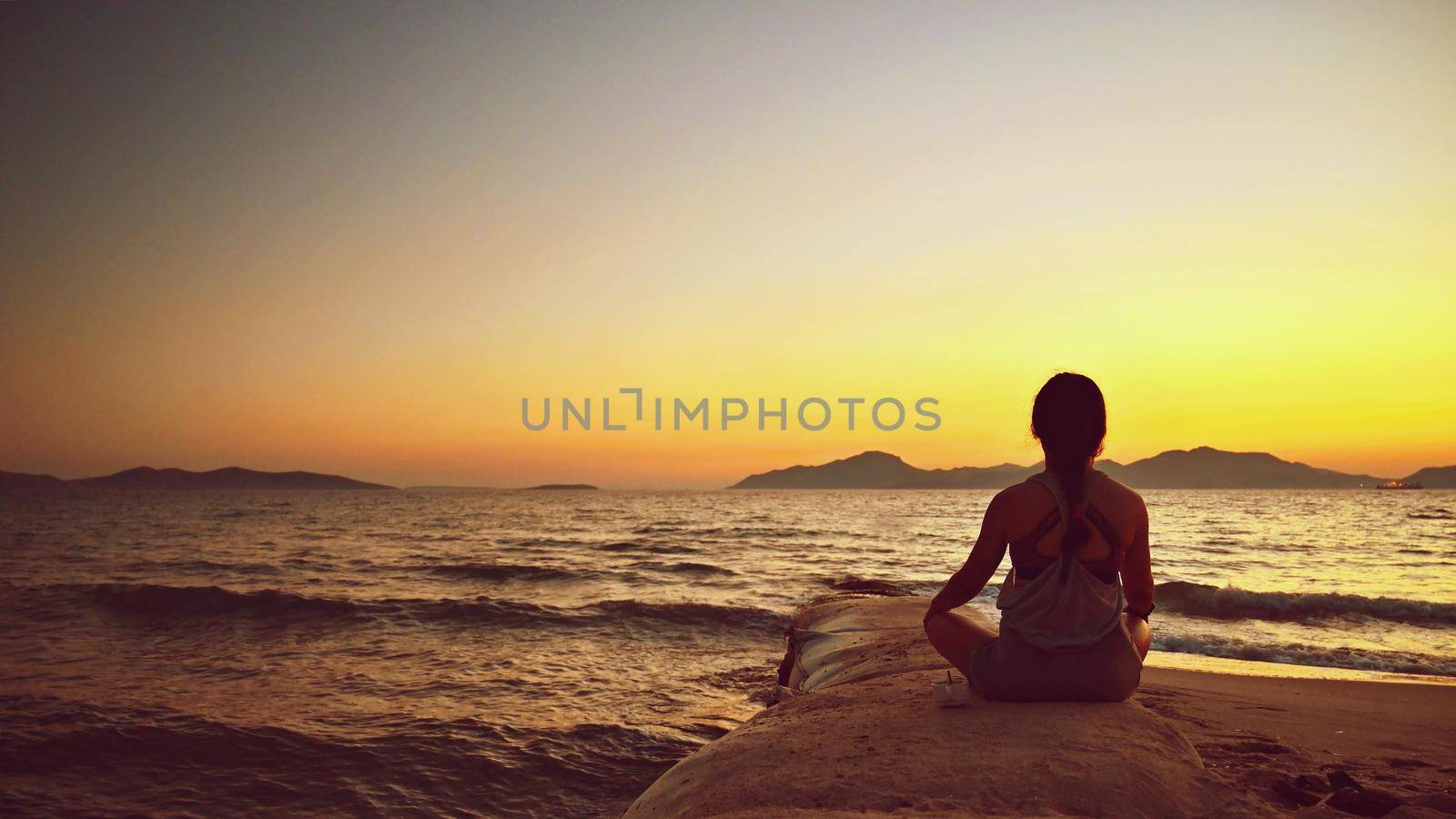 Woman meditates - relaxes at sunset by the sea on the beach. Concept for yoga, health and spa. by Montypeter