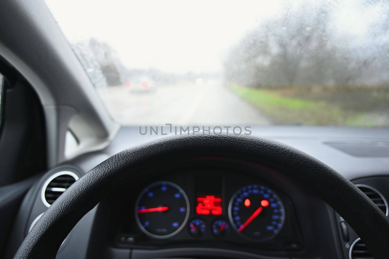View from the driver - car interior with steering wheel and dashboard. Winter bad rainy weather and dangerous driving on the road.