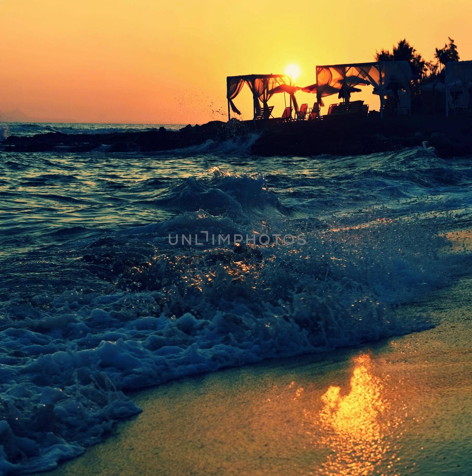 Beautiful summer sunset by the sea. Amazing scenery on the beach with waves and reflection of the sun. Background for holiday and vacation travel. Greece Crete Island. by Montypeter