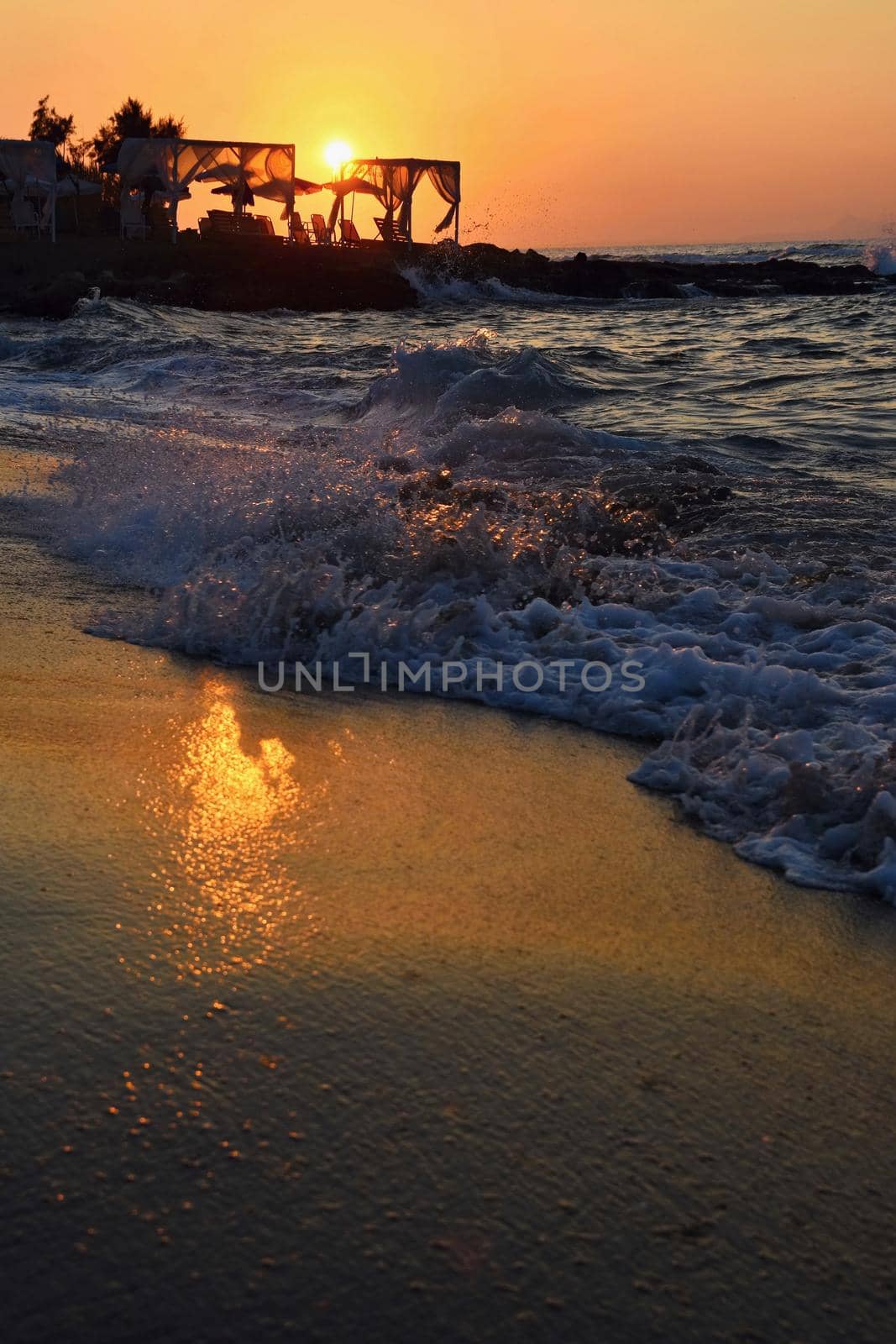 Beautiful summer sunset by the sea. Amazing scenery on the beach with waves and reflection of the sun. Background for holiday and vacation travel. Greece Crete Island. by Montypeter