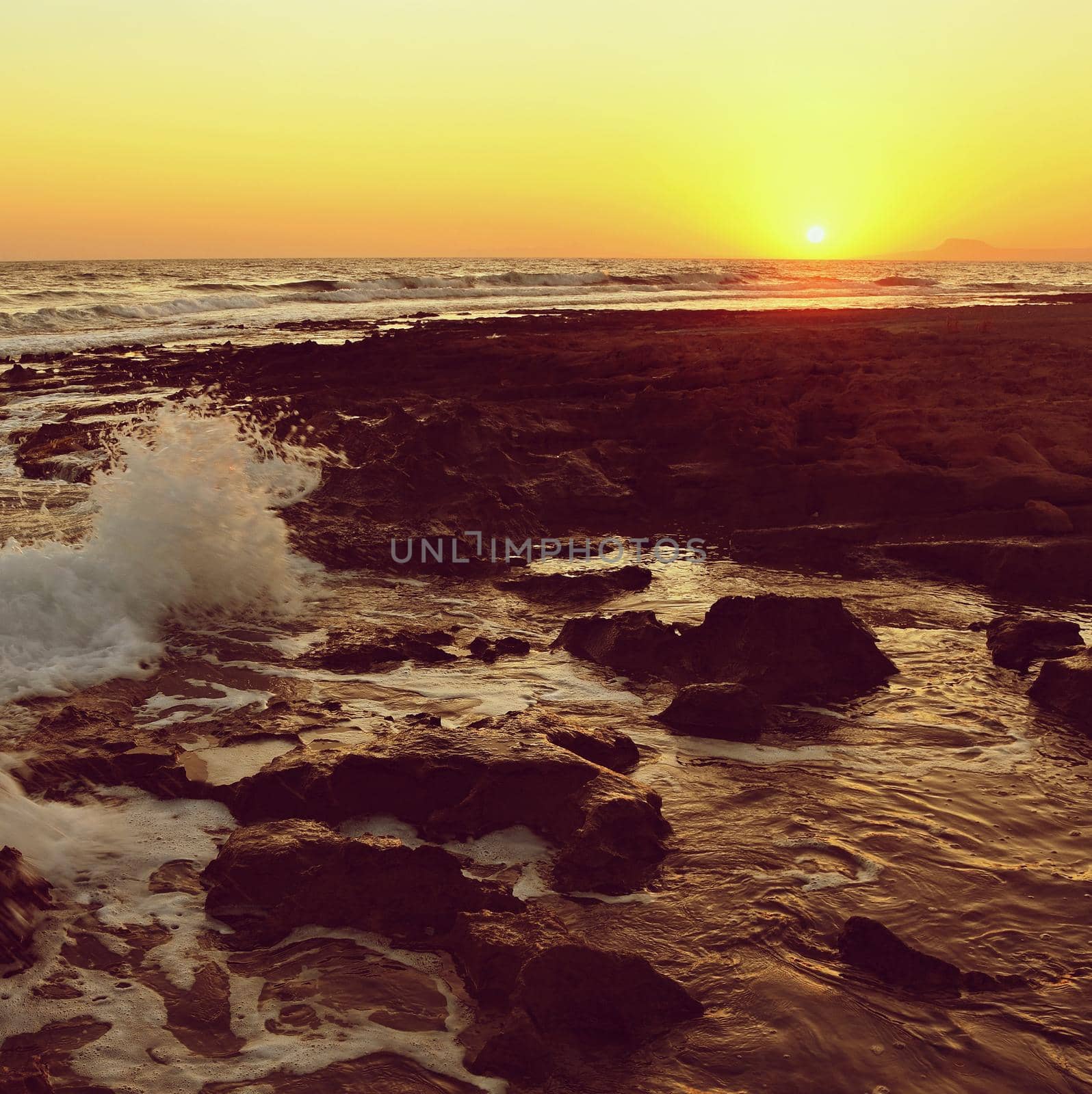 Beautiful summer sunset by the sea. Amazing scenery on the beach with waves and reflection of the sun. Background for holiday and vacation travel. Greece Crete Island.