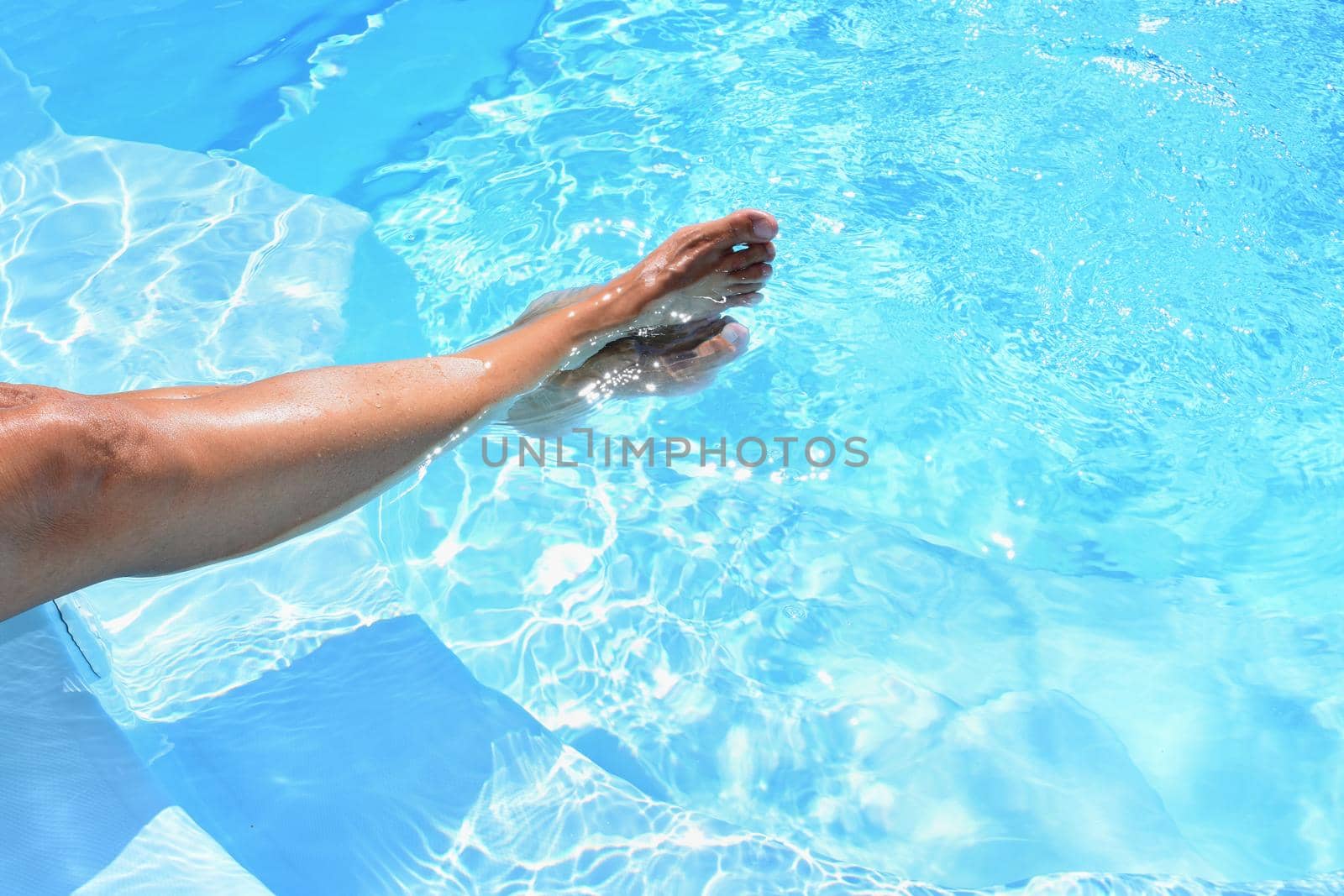 Legs in the pool with clean water in hot sunny day. Summer background for traveling and vacation. Holiday idyllic.