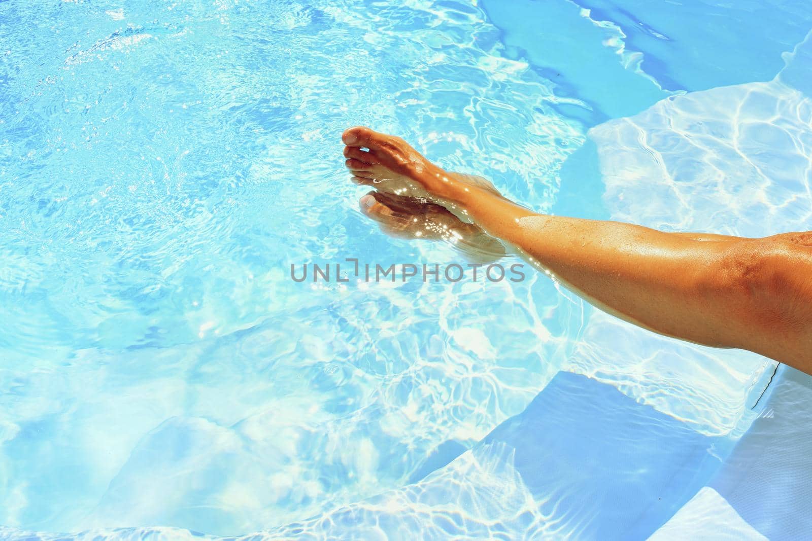 Legs in the pool with clean water in hot sunny day. Summer background for traveling and vacation. Holiday idyllic.
