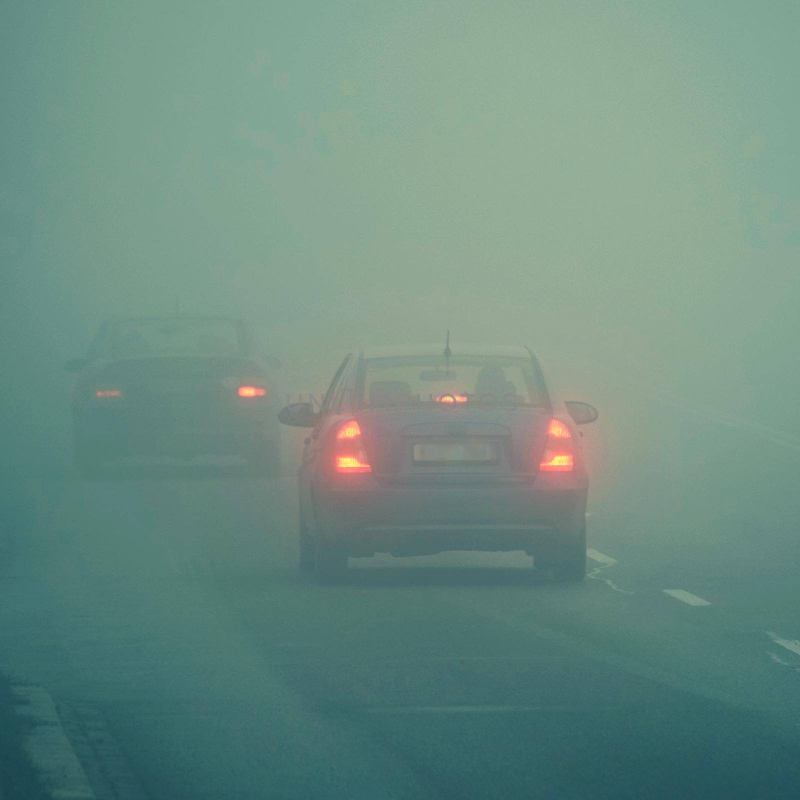 Cars in the fog. Bad winter weather and dangerous automobile traffic on the road. Light vehicles in fog. by Montypeter