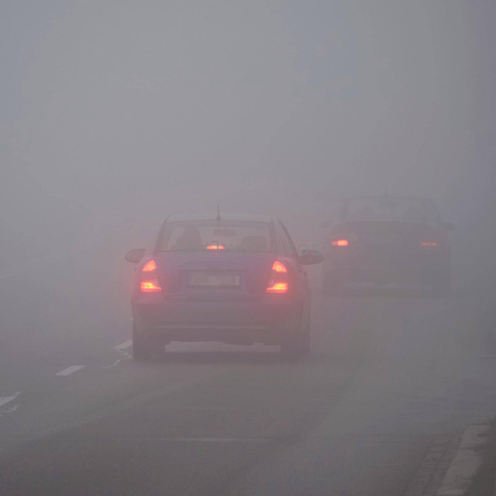 Cars in the fog. Bad winter weather and dangerous automobile traffic on the road. Light vehicles in fog.