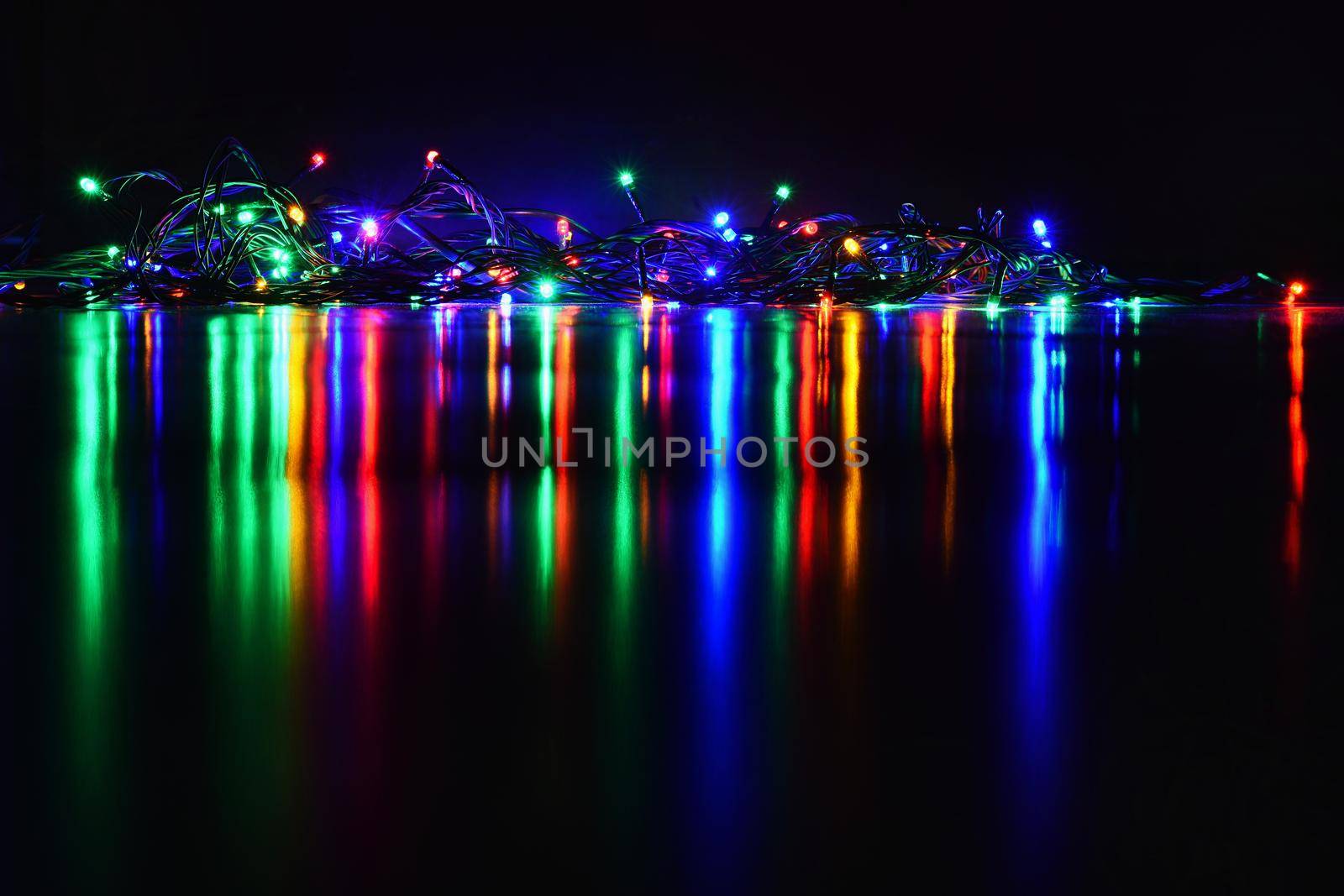 Christmas lights on black background with copy space. Colored reflecting surface.