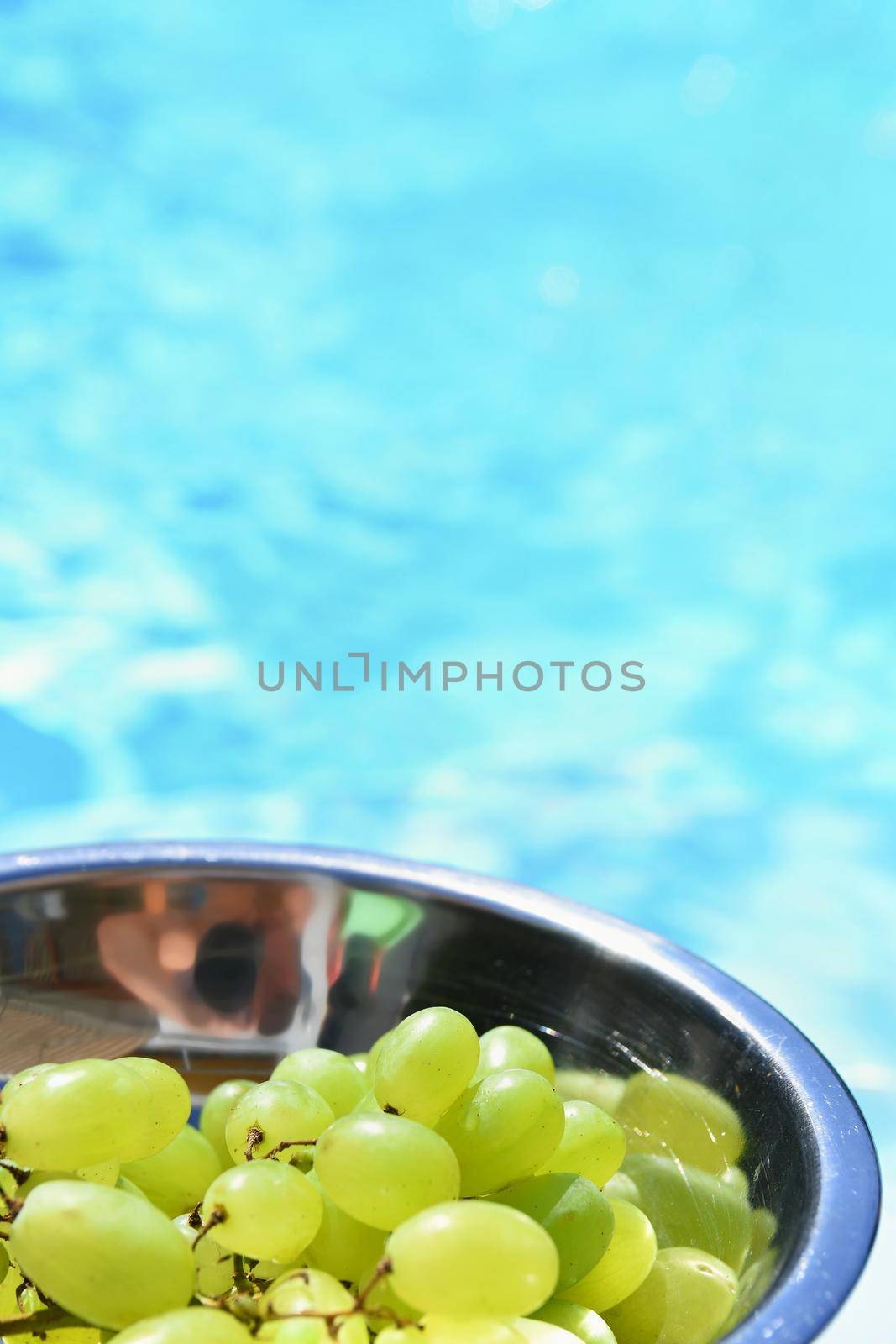 Grapes in a bowl with a background of blue water by Montypeter