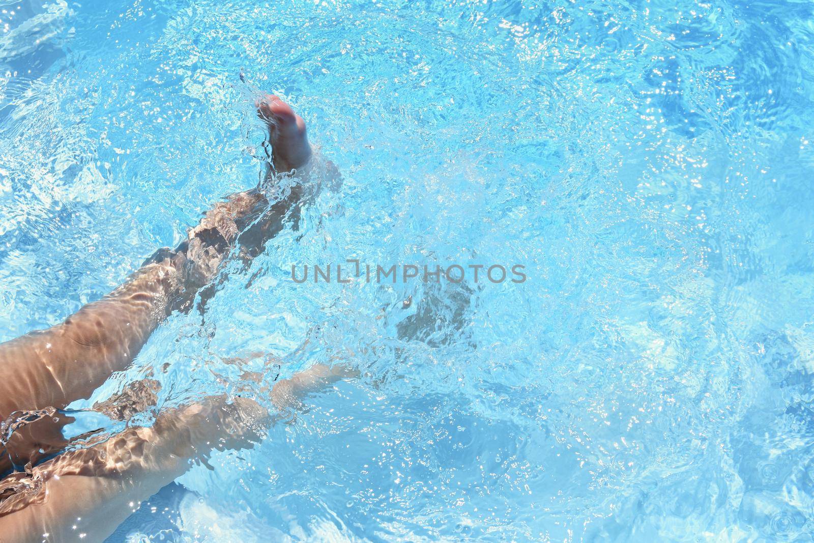 Children's feet in the water. Pool in the summer. Beautiful clear blue water and background for travel and holidays. by Montypeter