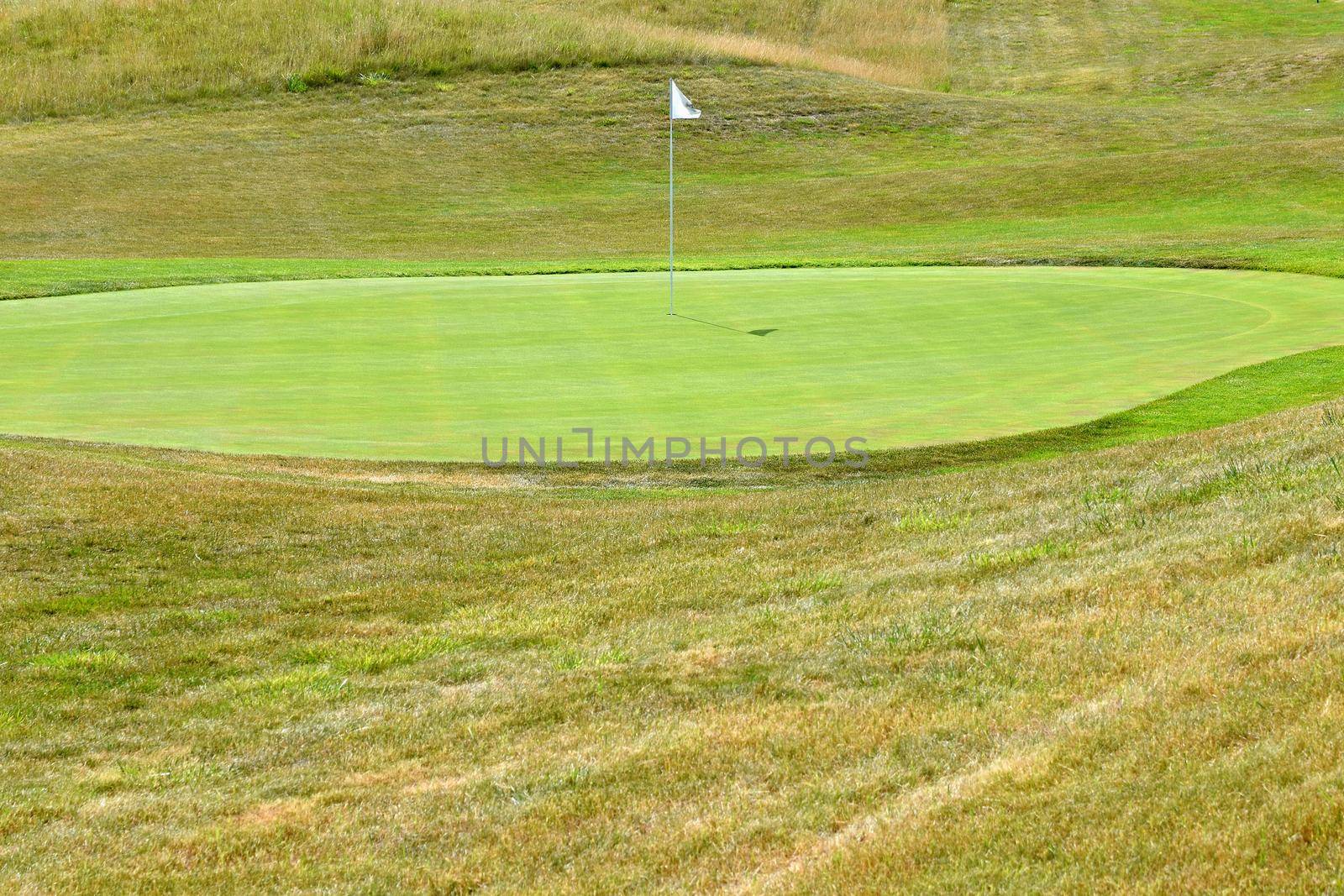 Nice golf course on a sunny summer day. Hole with a flag. Popular outdoor sport. by Montypeter