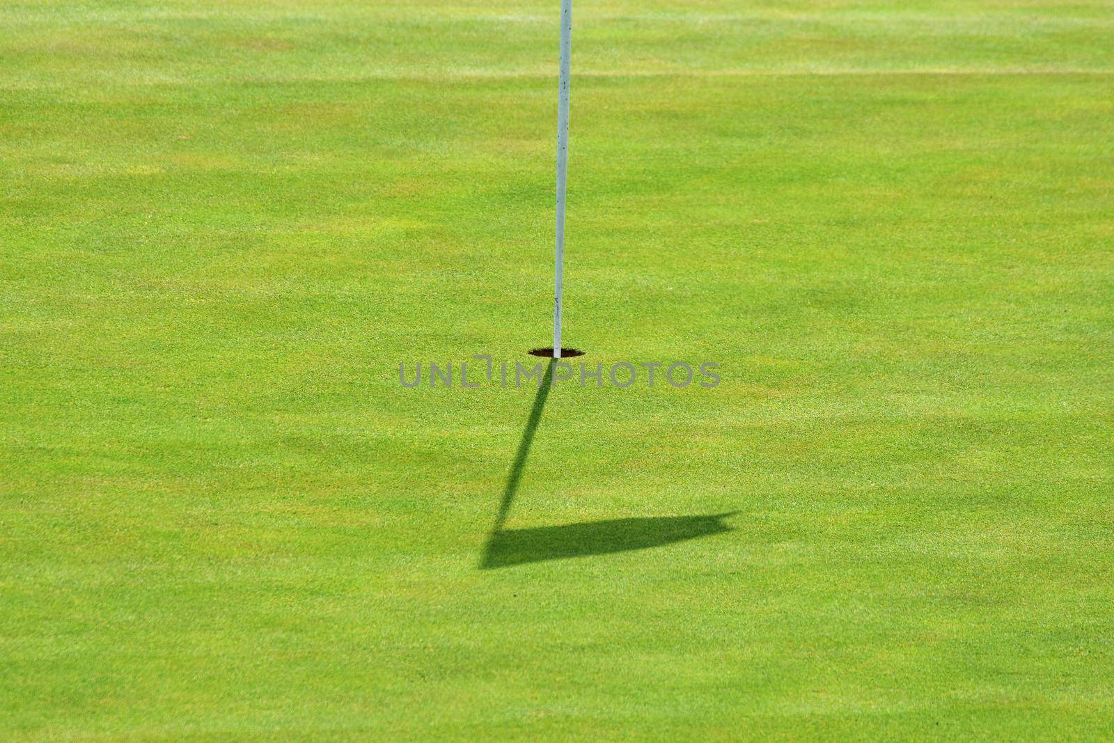 Nice golf course on a sunny summer day. Hole with a flag. Popular outdoor sport. by Montypeter