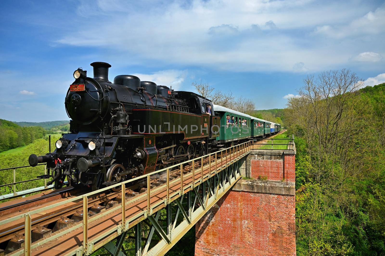 Brno, Czech republic, May 19th, 2019. Beautiful old steam train driving along a bridge in the countryside. Concept for travel, transportation and retro old style.
