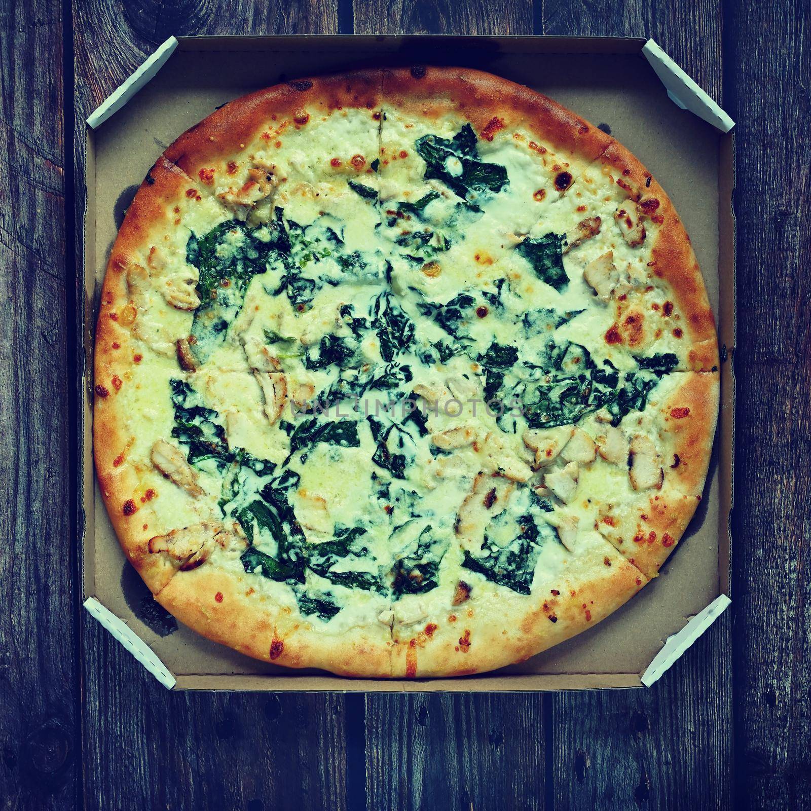 Delicious fresh pizza served on wooden table. Pizza with cream and spinach ready for delivery in a box.
