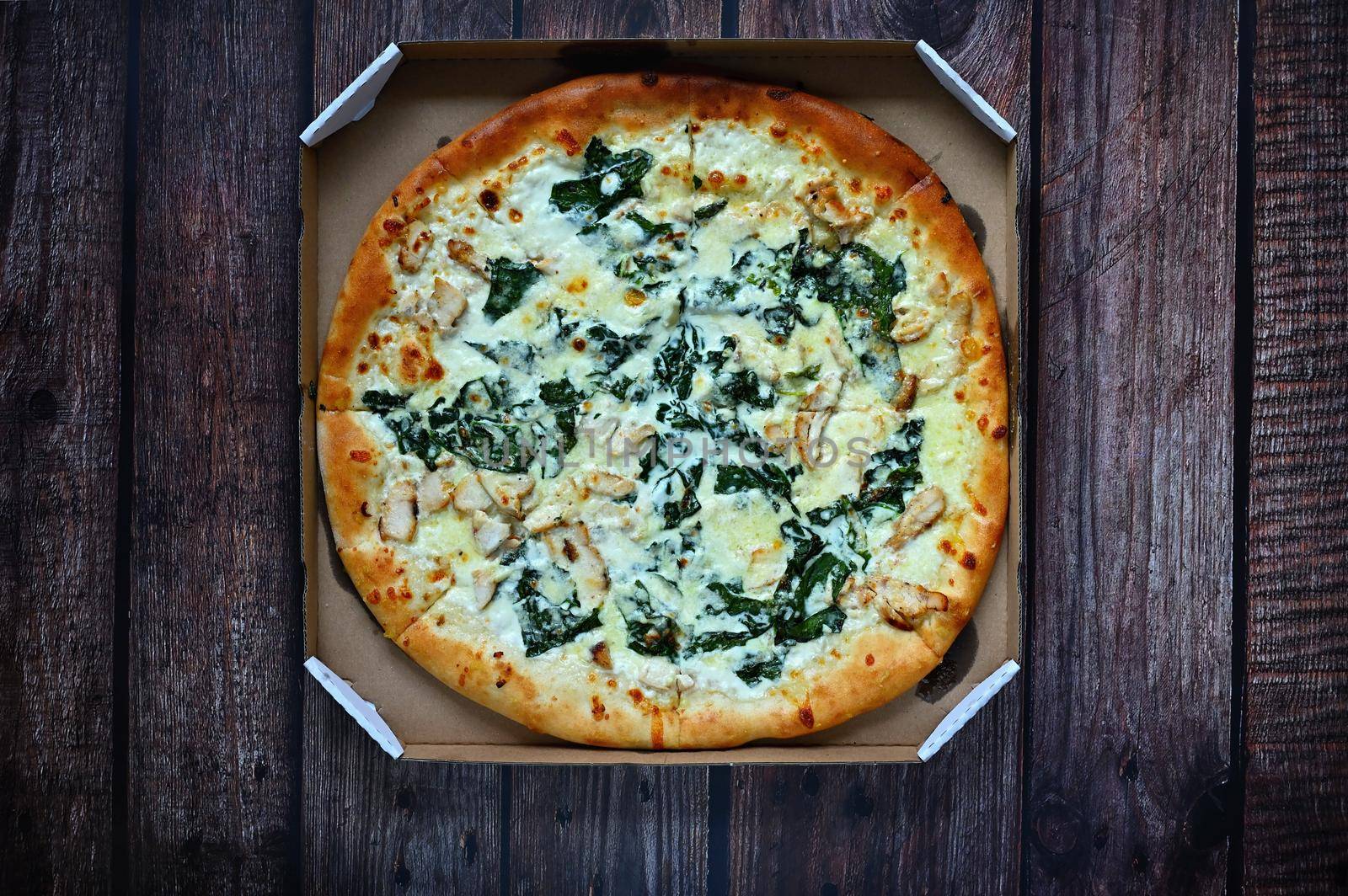 Delicious fresh pizza served on wooden table. Pizza with cream and spinach ready for delivery in a box. by Montypeter