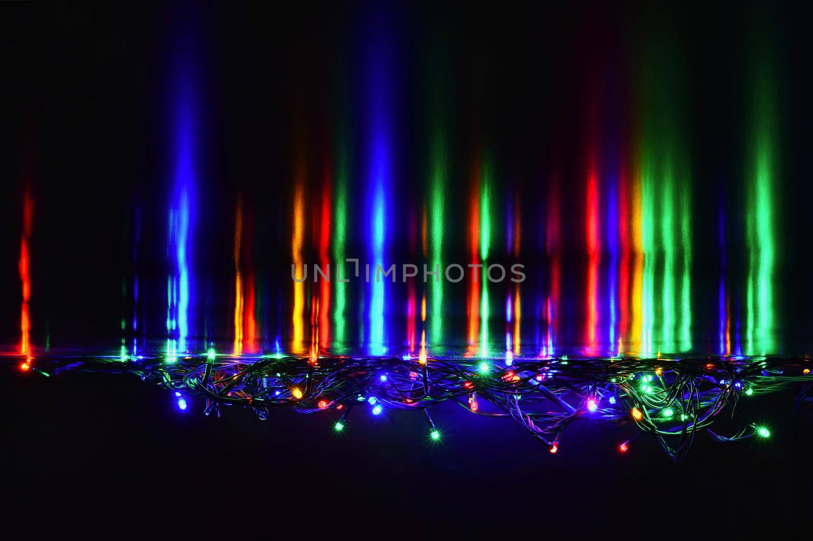 Christmas lights on black background with copy space. Colored reflecting surface.