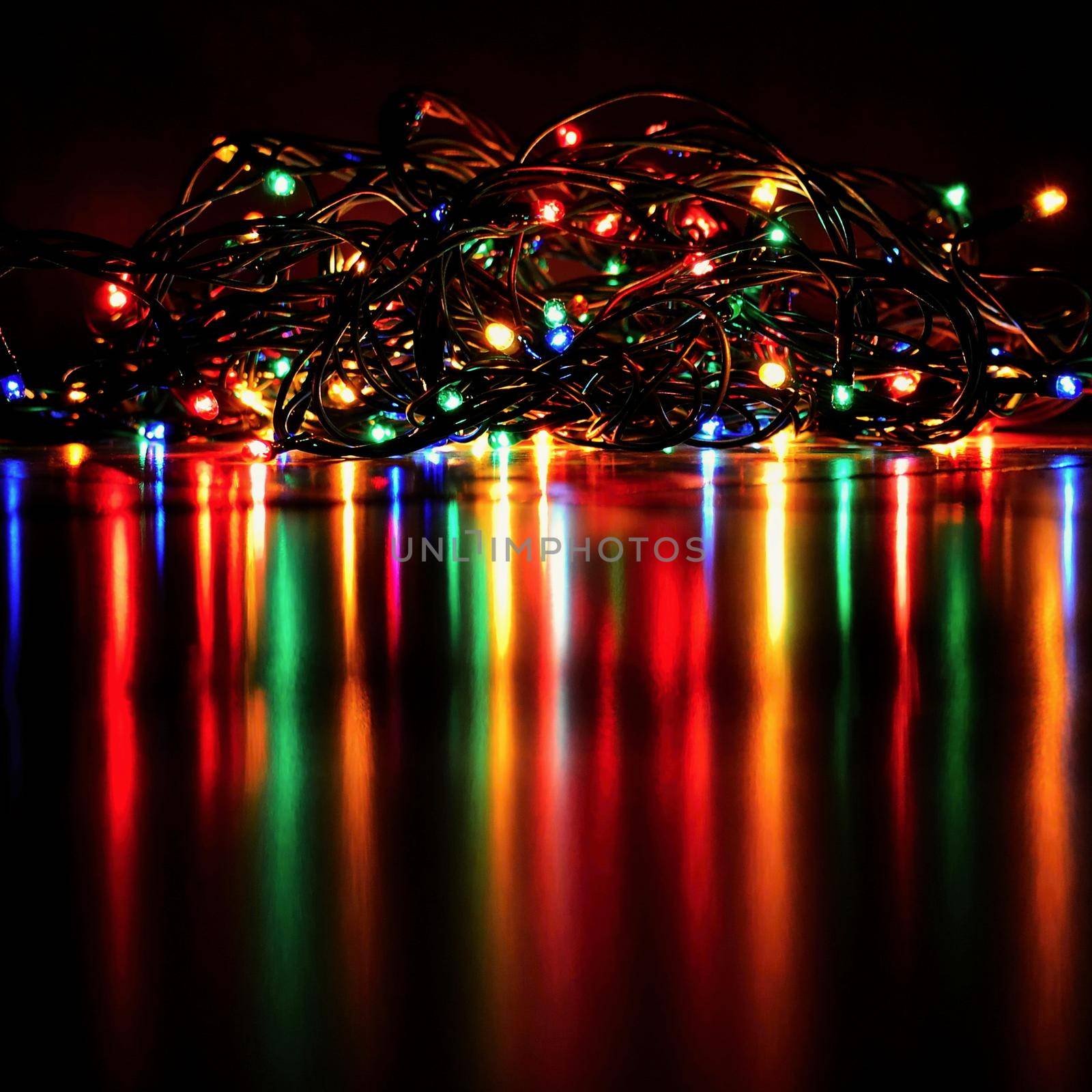 Christmas lights on black background with copy space. Colored reflecting surface. by Montypeter